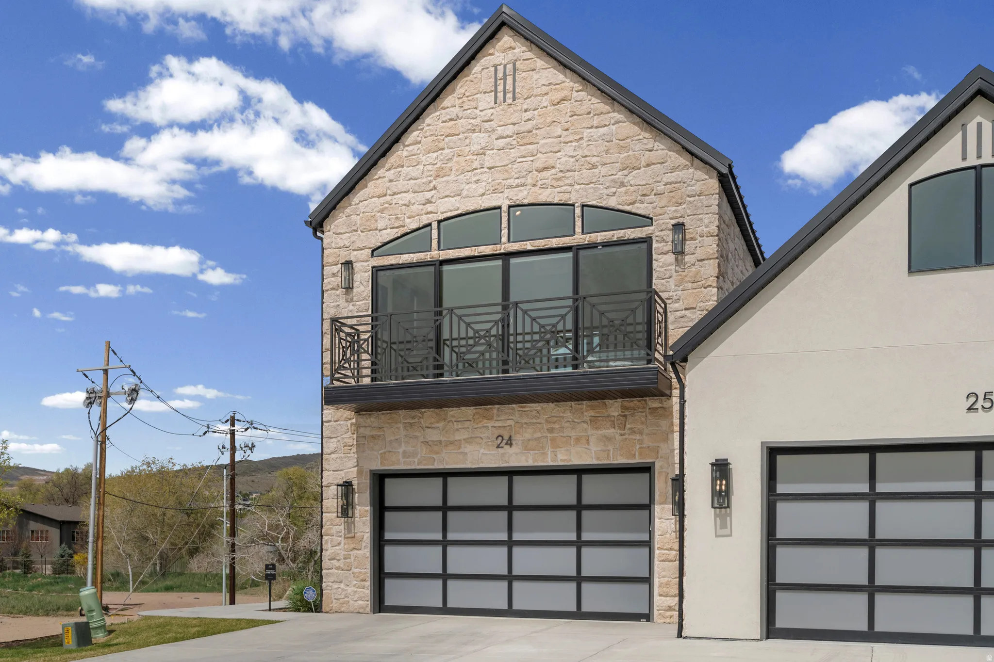 View of front of house featuring stone siding, concrete driveway, a garage, and a balcony