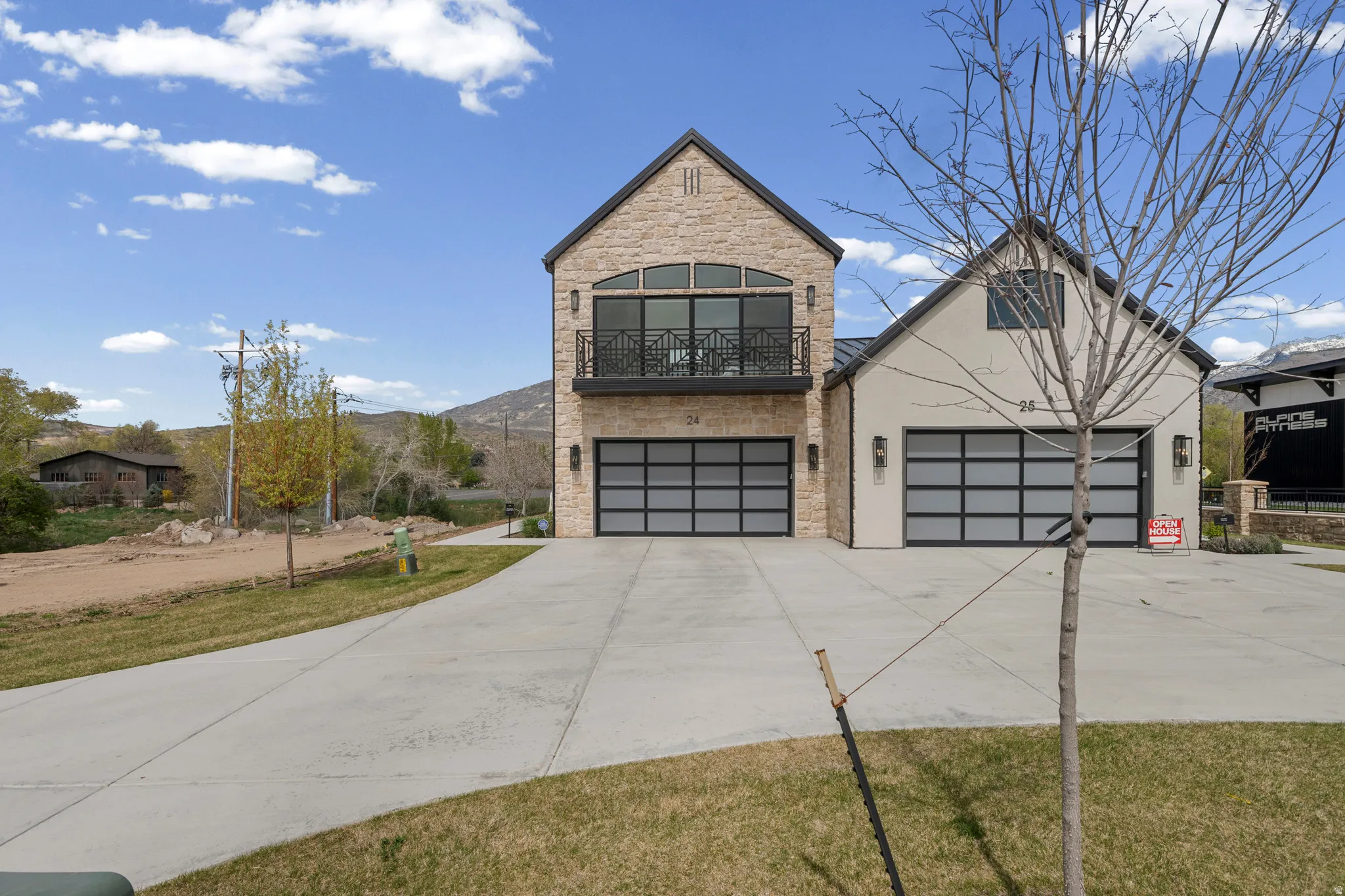 View of front of home featuring stone siding, driveway, a front yard, stucco siding, and a balcony