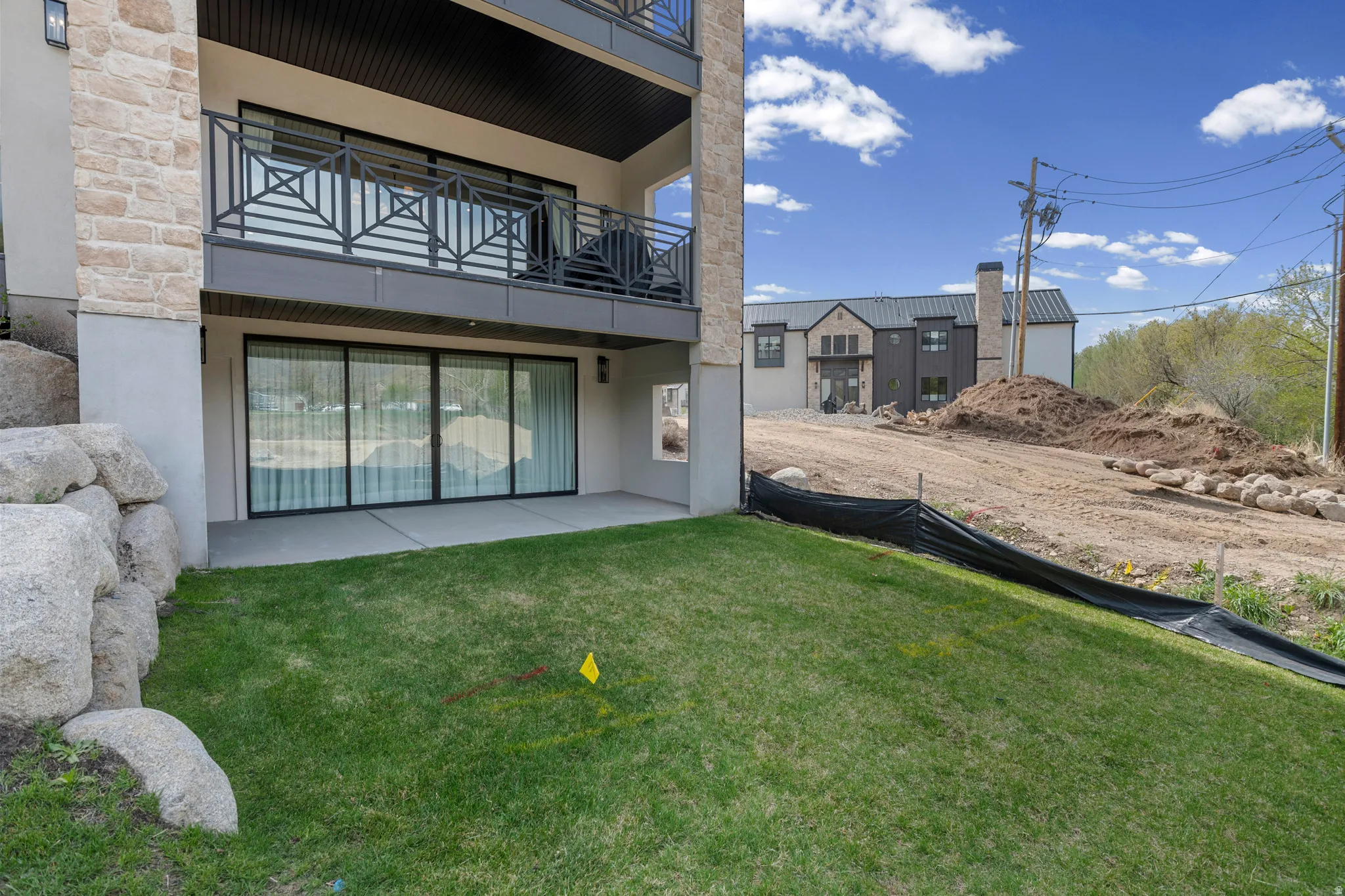 Rear view of house with a patio area, a balcony, stucco siding, a lawn, and stone siding