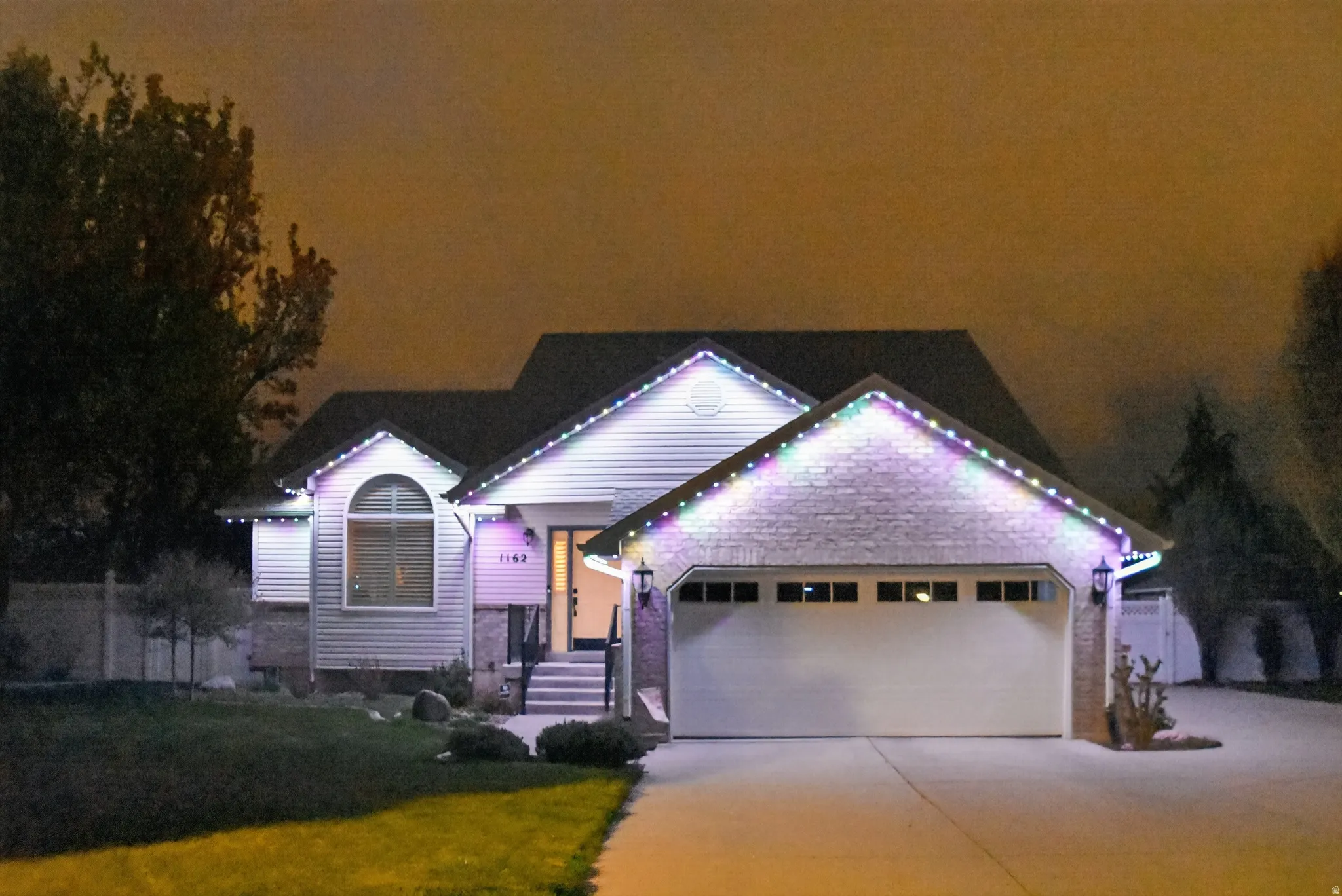 View of front of home featuring an attached garage, concrete driveway, brick siding, and a lawn