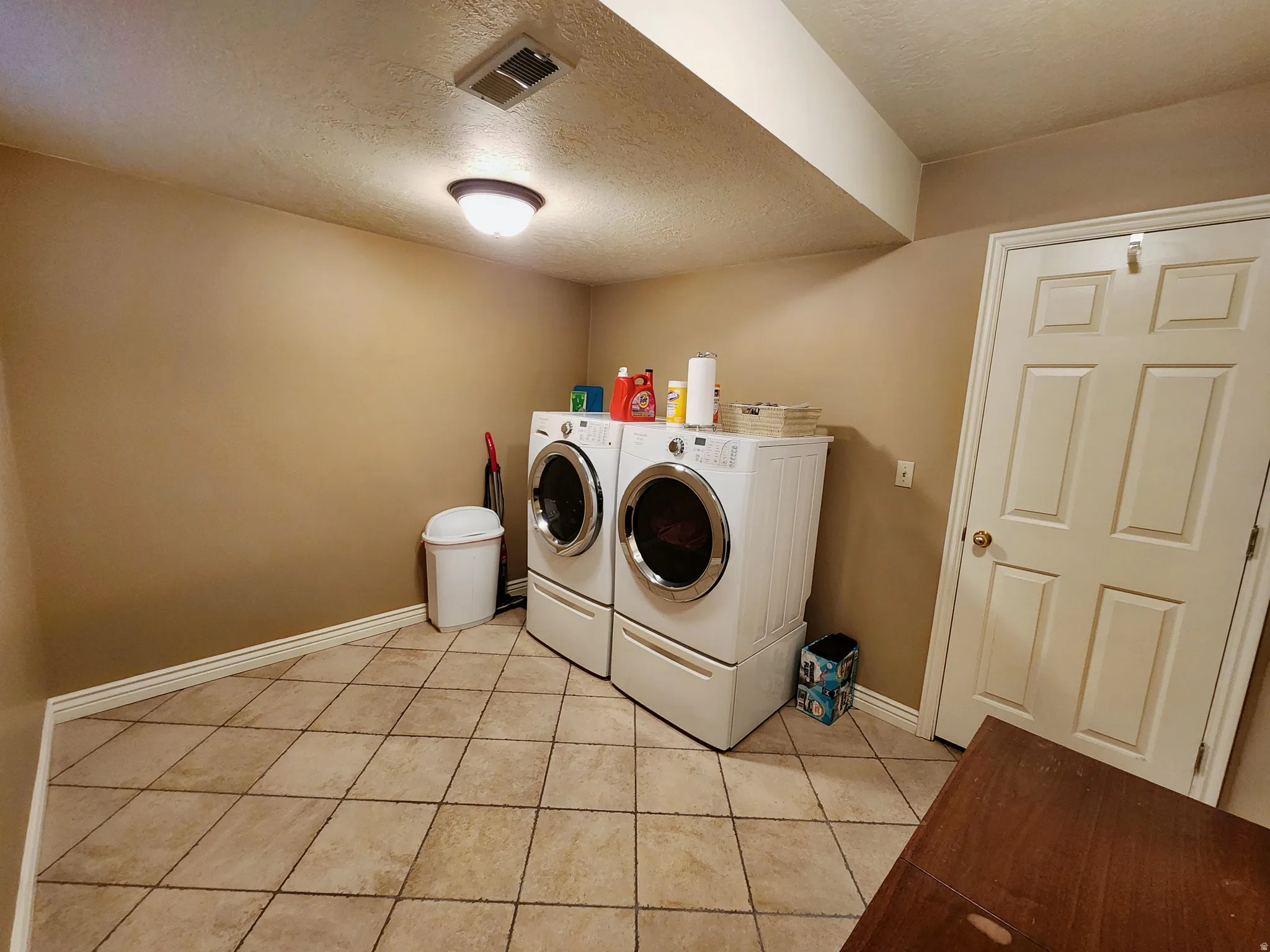 Laundry room with a textured ceiling, light tile patterned floors, and washer and clothes dryer