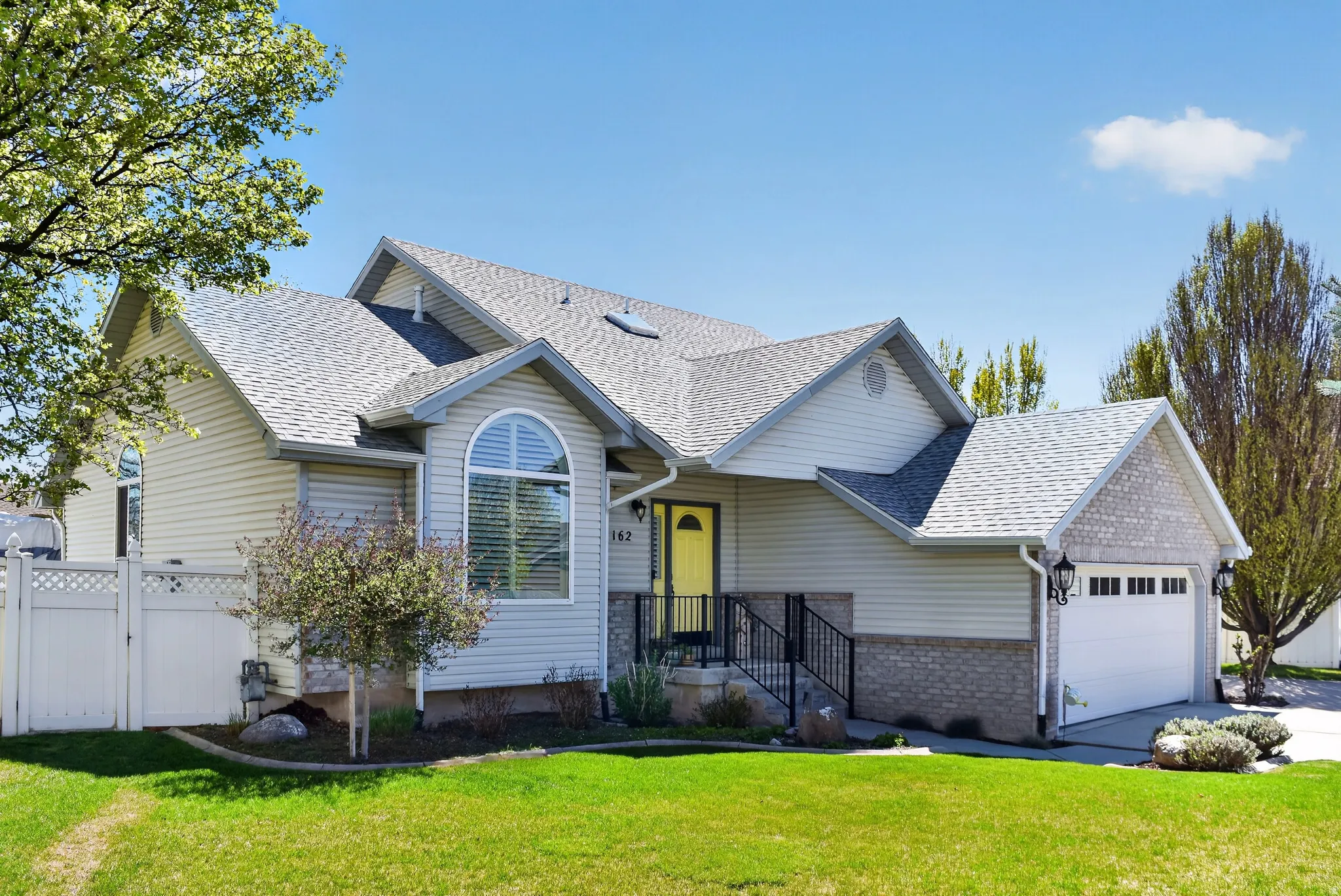 View of front of house featuring roof with shingles, an attached garage, brick siding, a gate, and driveway