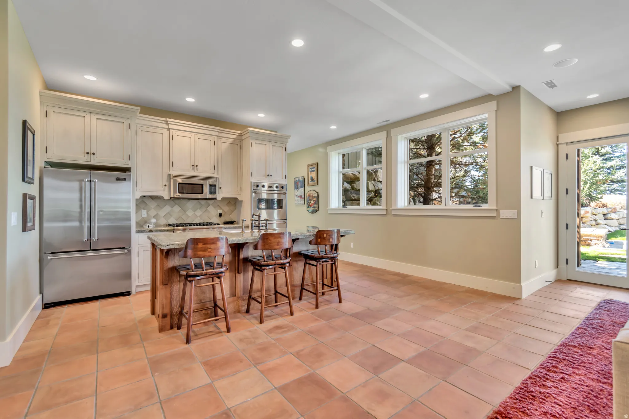 Kitchen with stainless steel appliances, light stone countertops, a kitchen island with sink, a kitchen breakfast bar, and light tile patterned floors