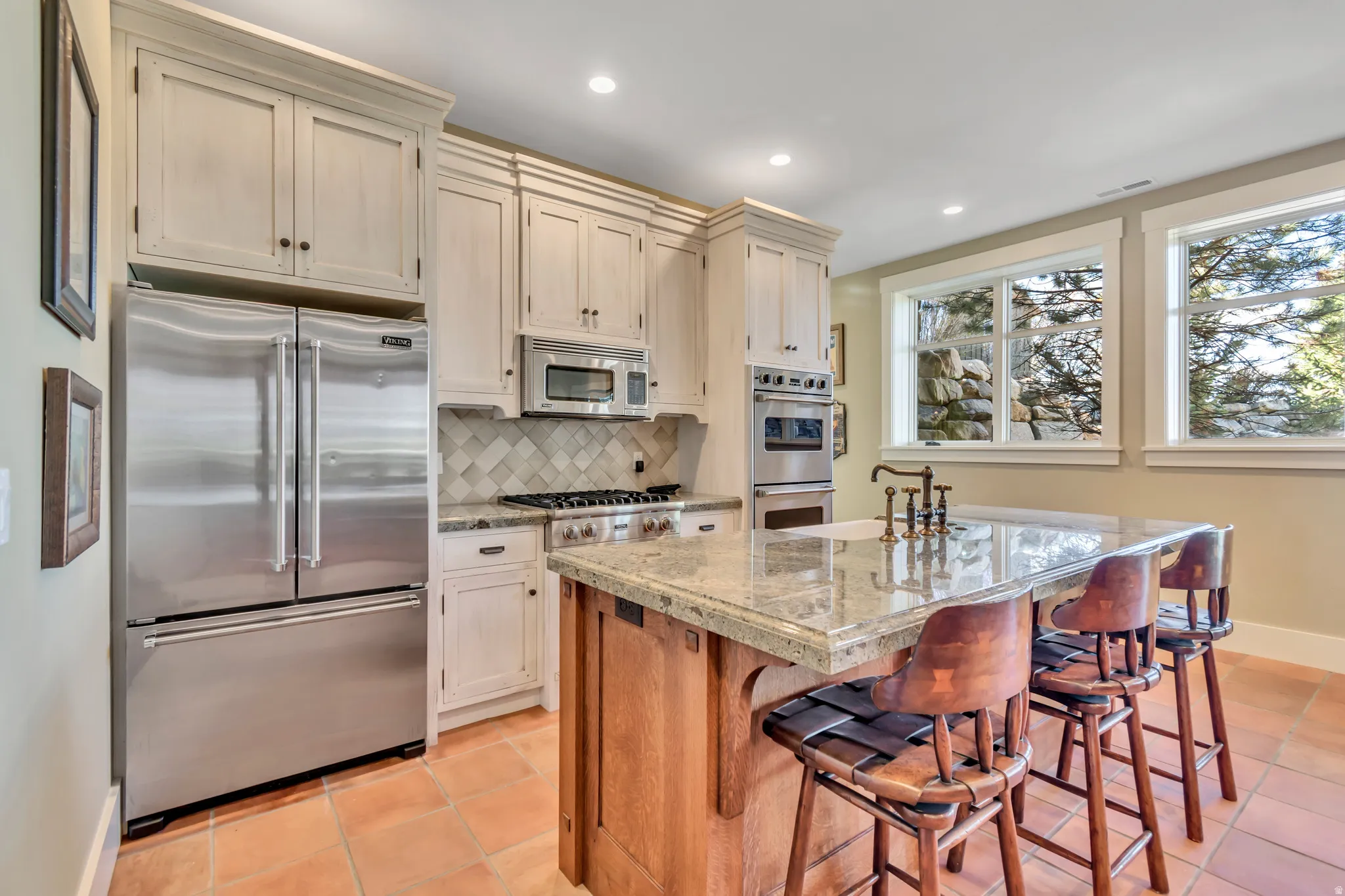 Two tone kitchen with stainless steel appliances, tasteful backsplash, a center island with sink, a kitchen bar, and recessed lighting