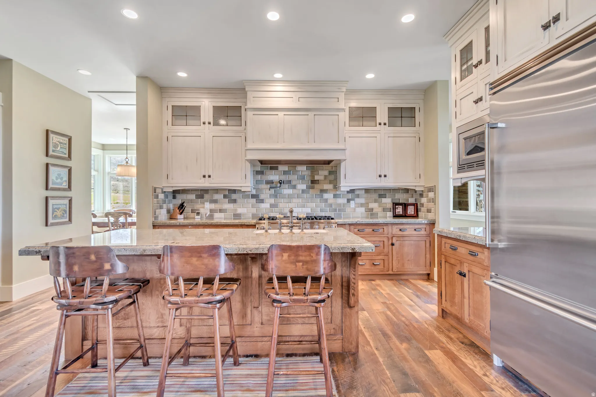 Kitchen with glass fronted cabinets, built in appliances, a center island with sink, light wood-style floors, and a kitchen bar
