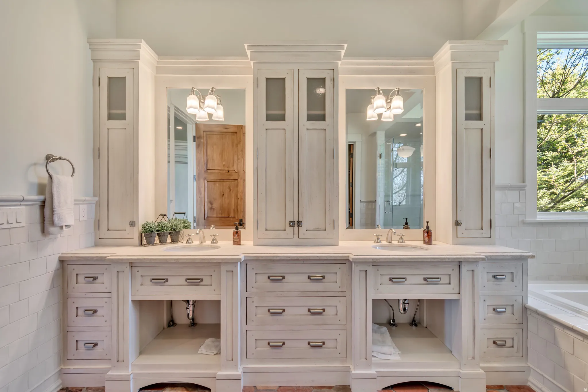 Bathroom featuring double vanity, suspended lighting, tile walls, a garden tub, and a wainscoted wall
