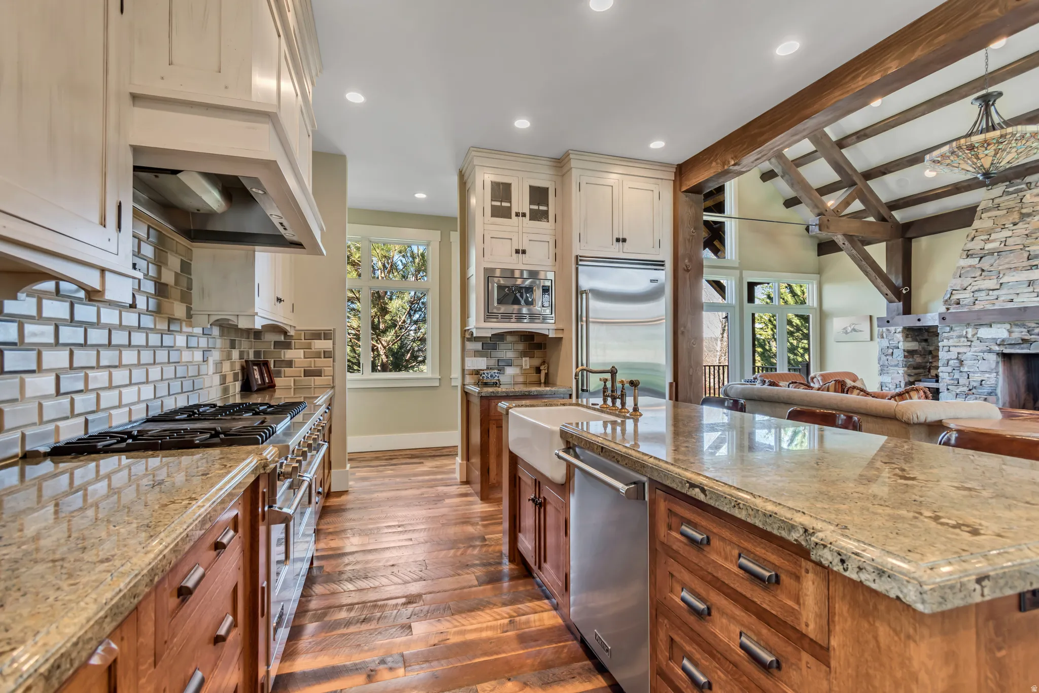 Dual tone kitchen with open floor plan, a stone fireplace, dark wood-type flooring, light stone countertops, and built in appliances