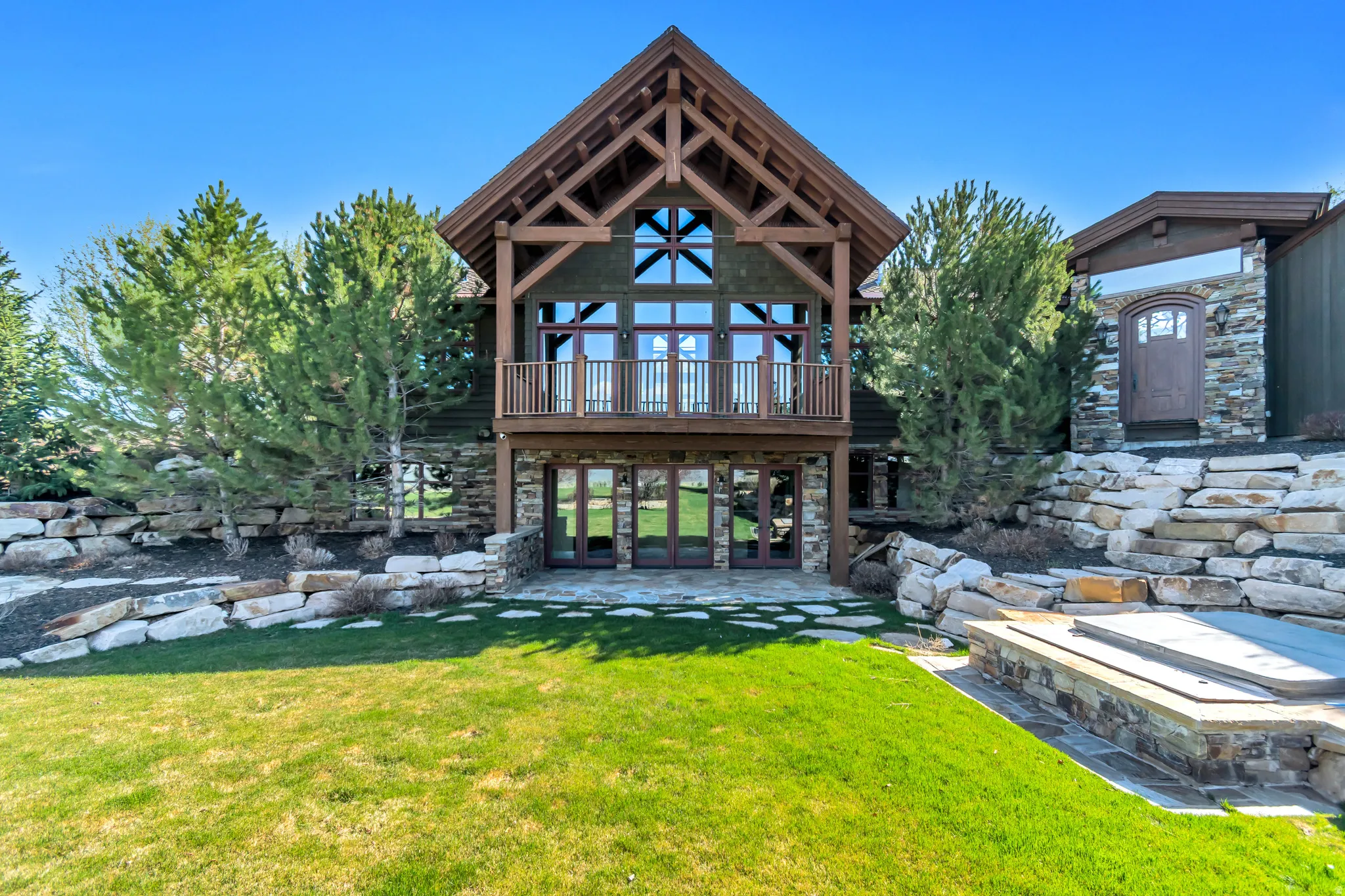 Rear view of property with a lawn, a patio area, stone siding, and french doors