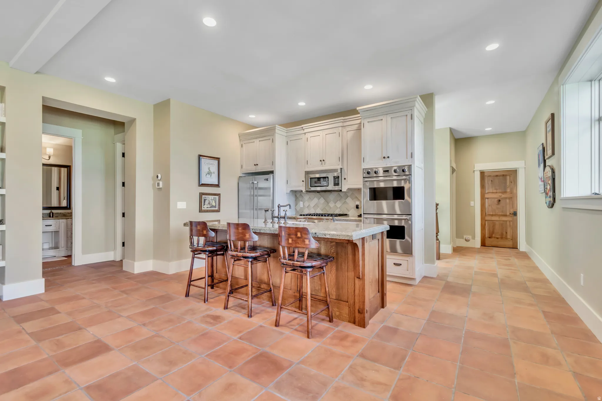 Kitchen with stainless steel appliances, an island with sink, a breakfast bar, light stone counters, and decorative backsplash