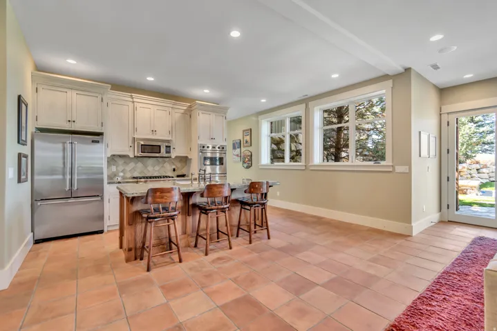 Kitchen with stainless steel appliances, light stone countertops, a kitchen island with sink, a kitchen breakfast bar, and light tile patterned floors