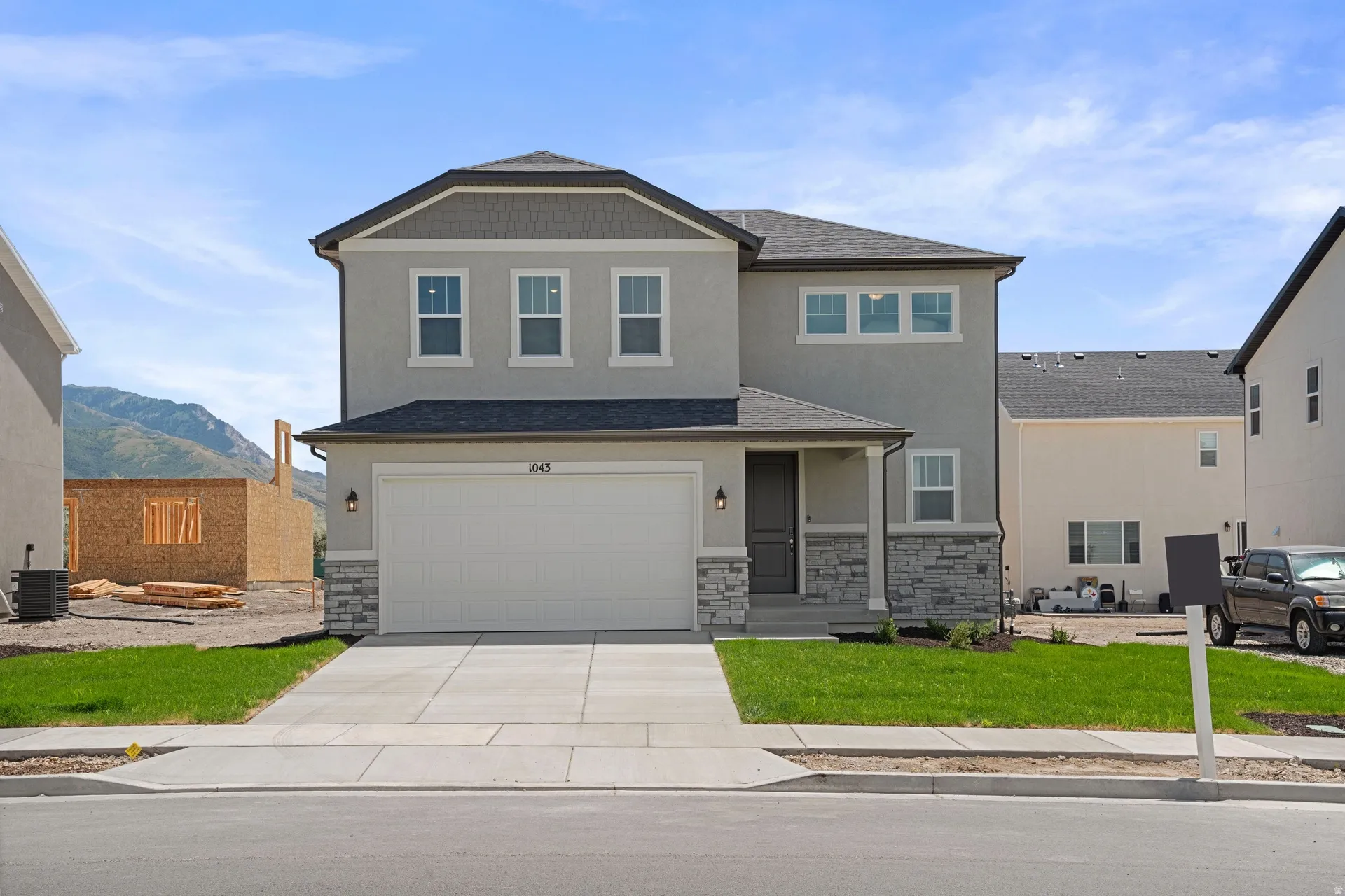 Contemporary two-story residence featuring a gray stucco exterior with stone accents, a two-car garage, dark trim, and a covered entry