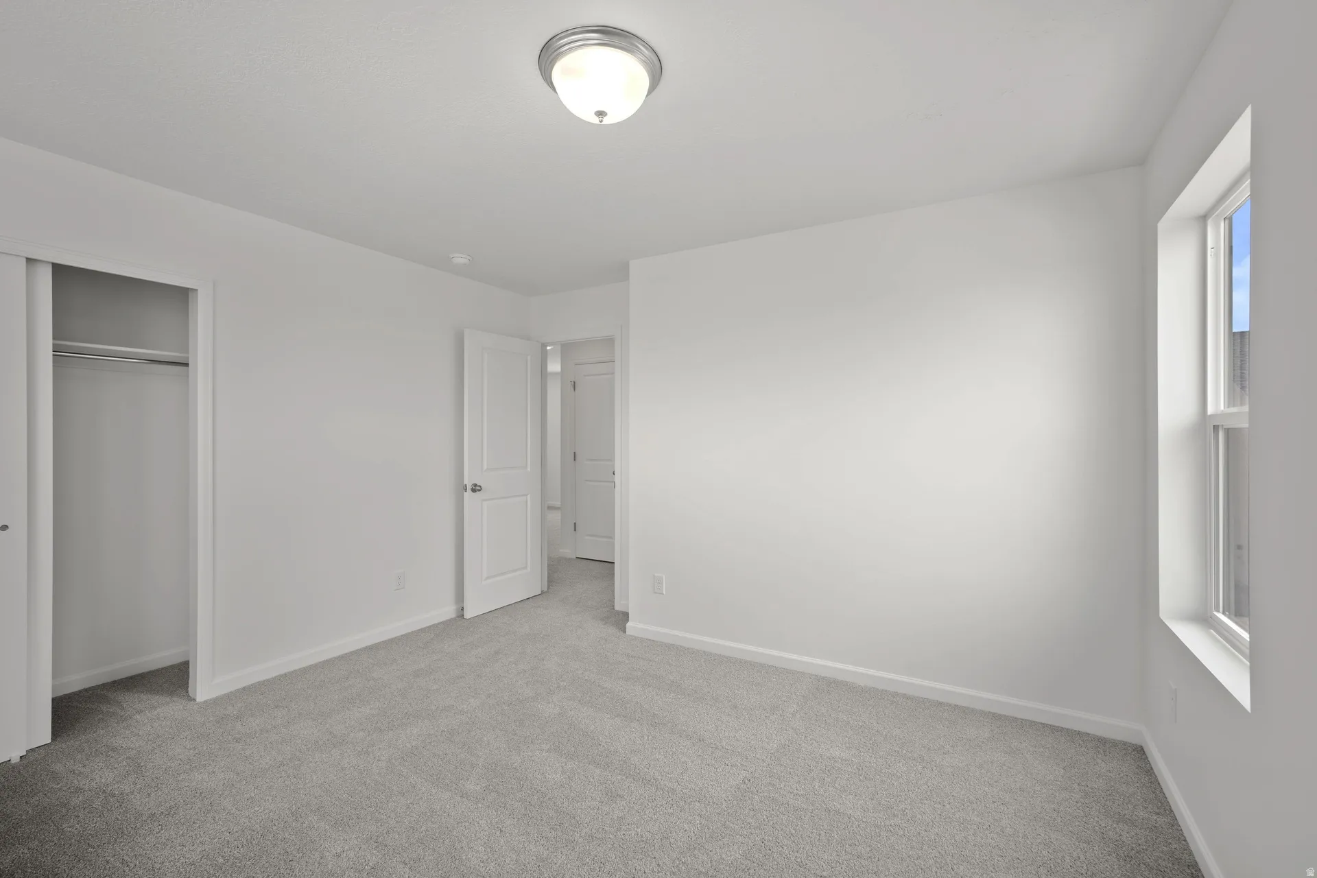 Bright bedroom featuring light gray carpet flooring, white walls, a single window, and a sliding closet