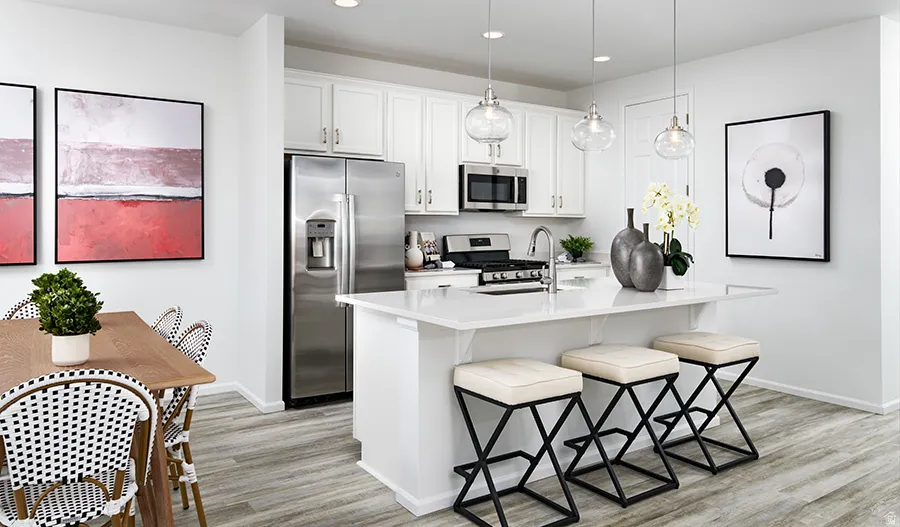 Kitchen with stainless steel appliances, white cabinets, a breakfast bar, an island with sink, and light wood-style flooring