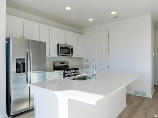 Kitchen with stainless steel appliances, white cabinets, a center island with sink, light wood finished floors, and recessed lighting