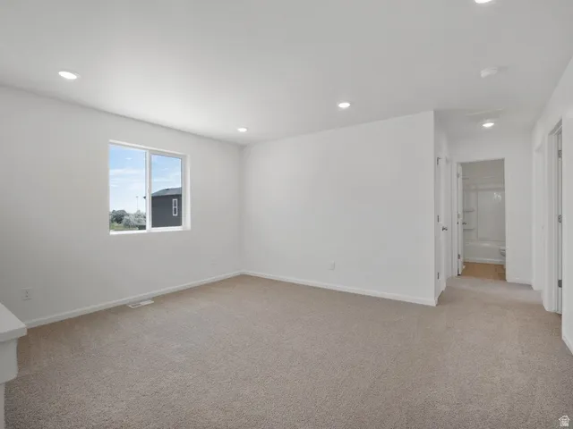 Bright interior space featuring light beige carpeting, white walls, a single pane window, and recessed lighting