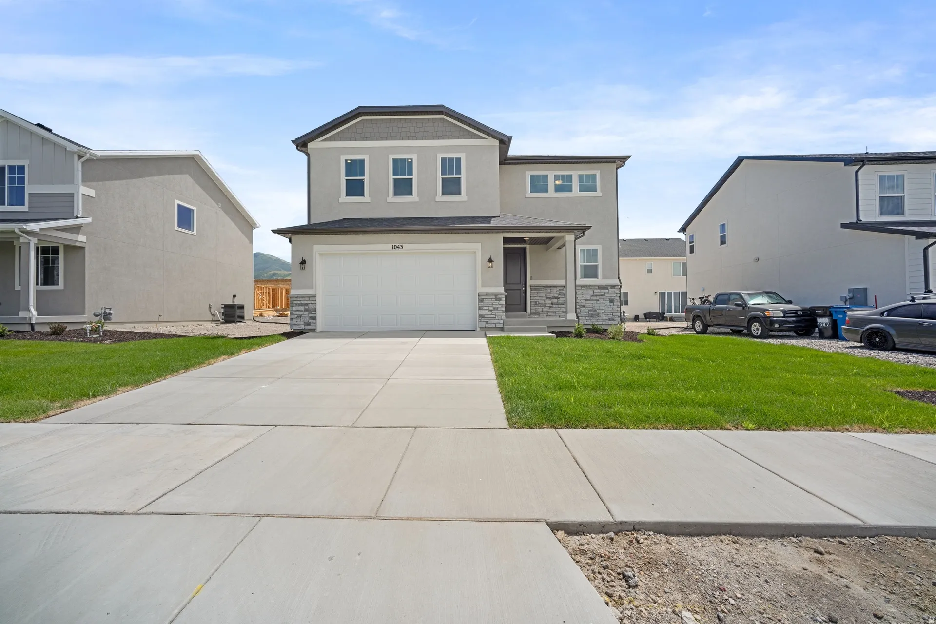 Contemporary two-story residence featuring a two-car garage, stone and stucco exterior, covered entry, and a manicured lawn