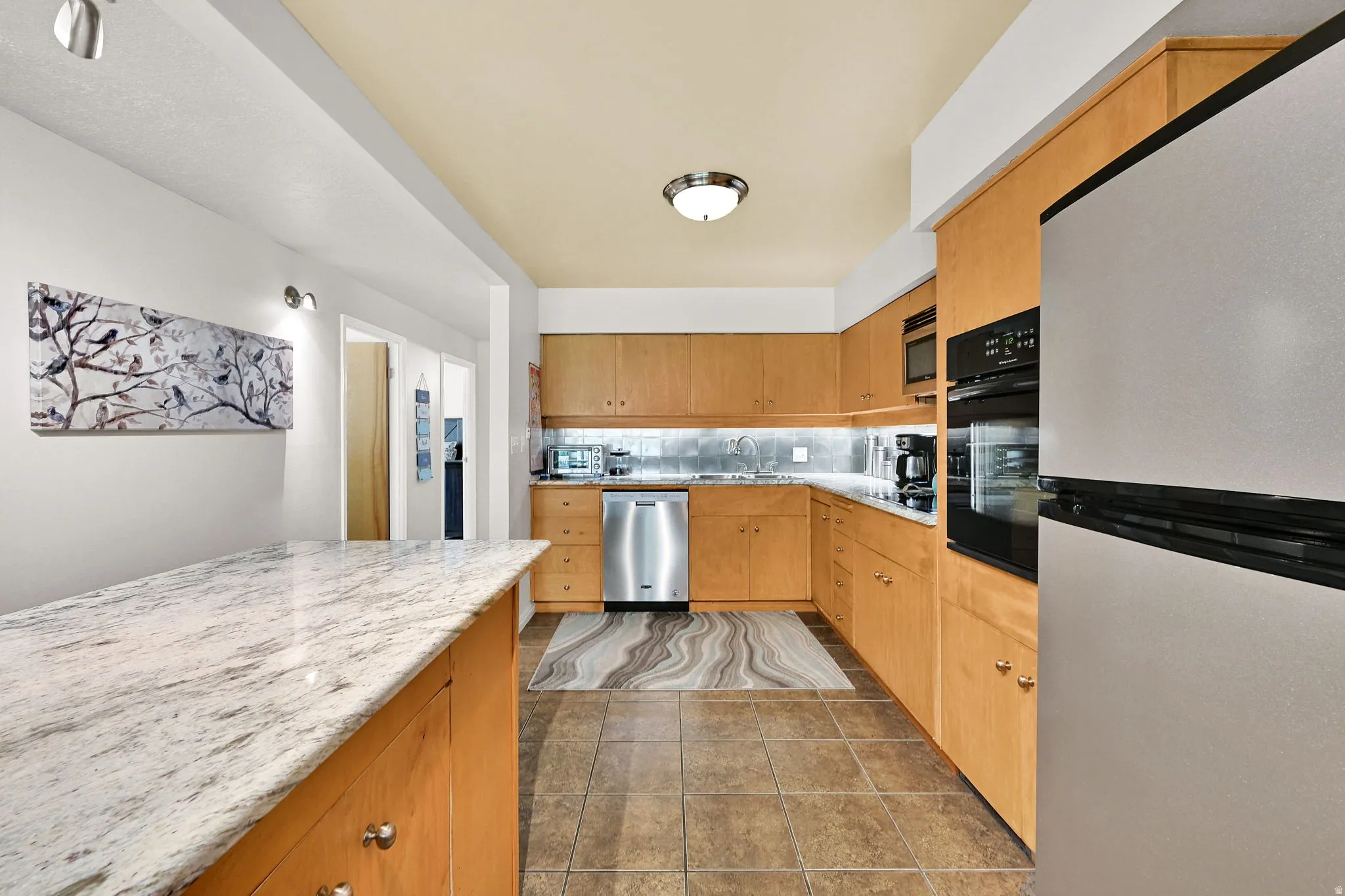 Kitchen featuring stainless steel appliances, tasteful backsplash, and light stone counters