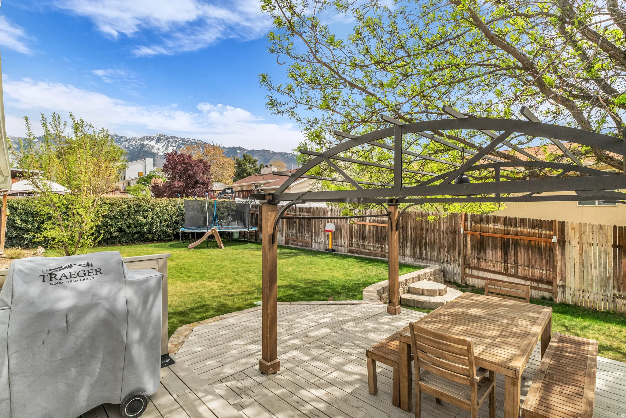 Fenced backyard featuring a trampoline, outdoor dining space, a patio, and a deck with mountain view