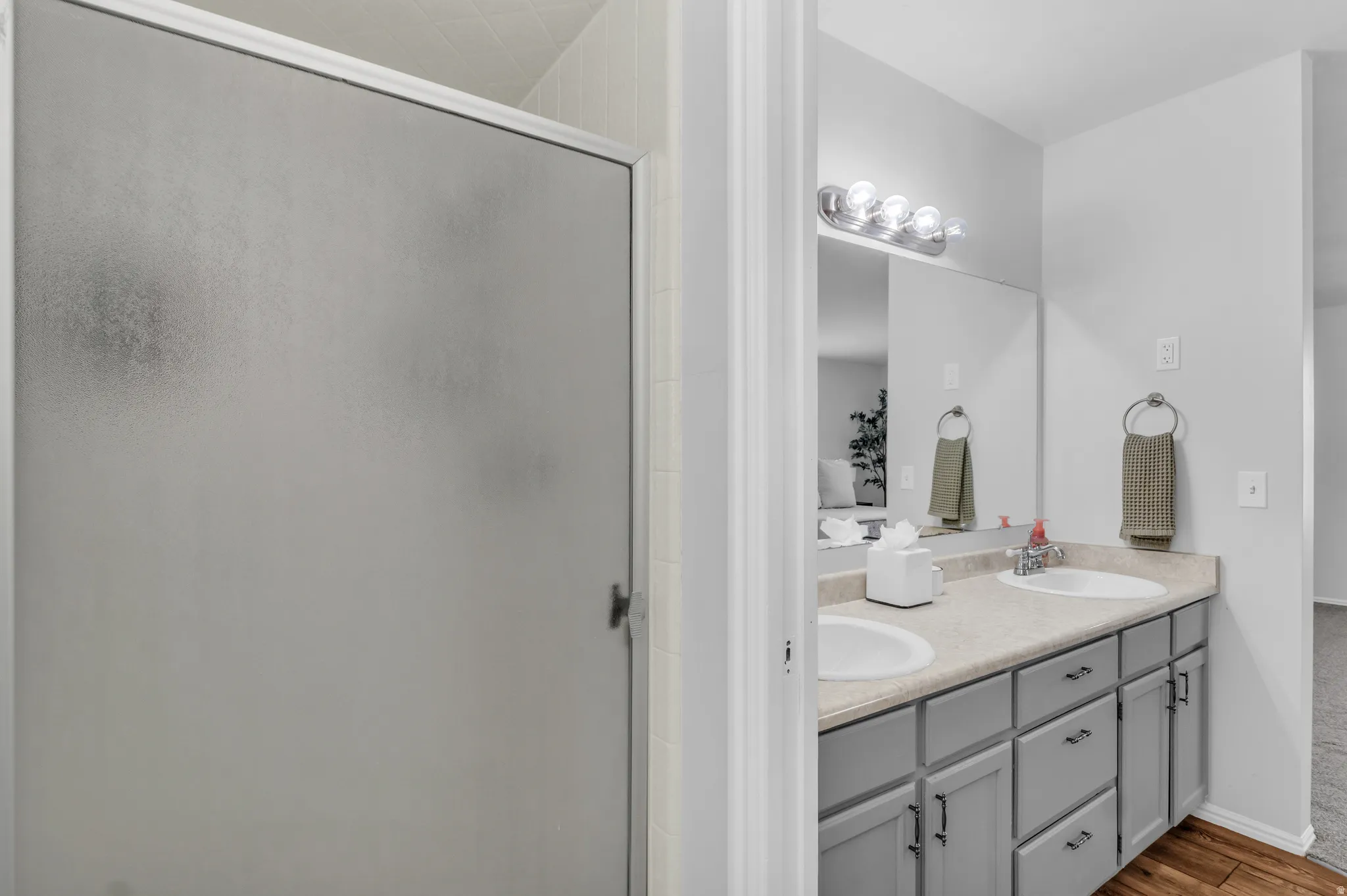 Bathroom with double vanity, light wood-type flooring, and a stall shower