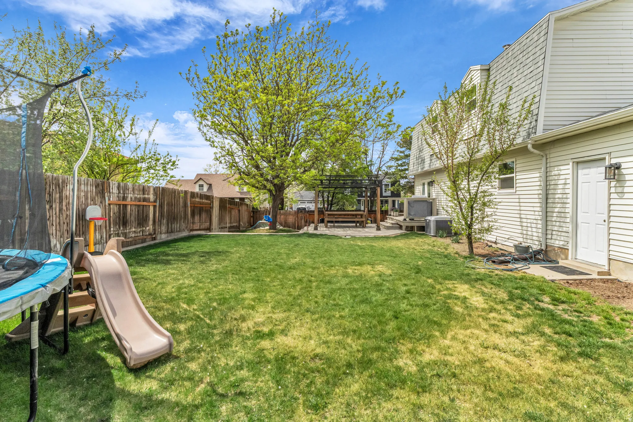 Fenced backyard featuring a trampoline, a patio area, a deck, and a pergola.