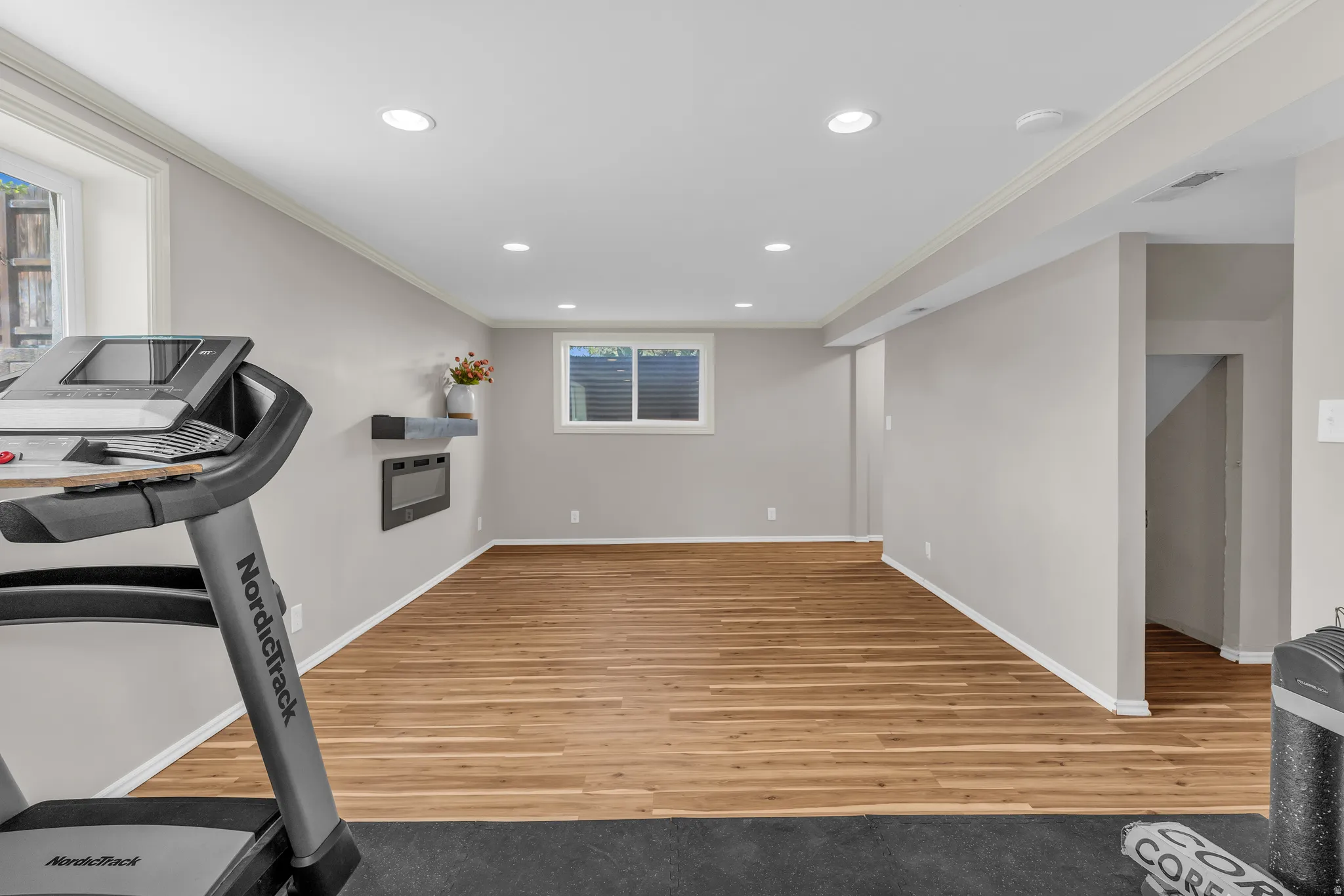 Exercise room with light wood finished floors, crown molding, and recessed lighting