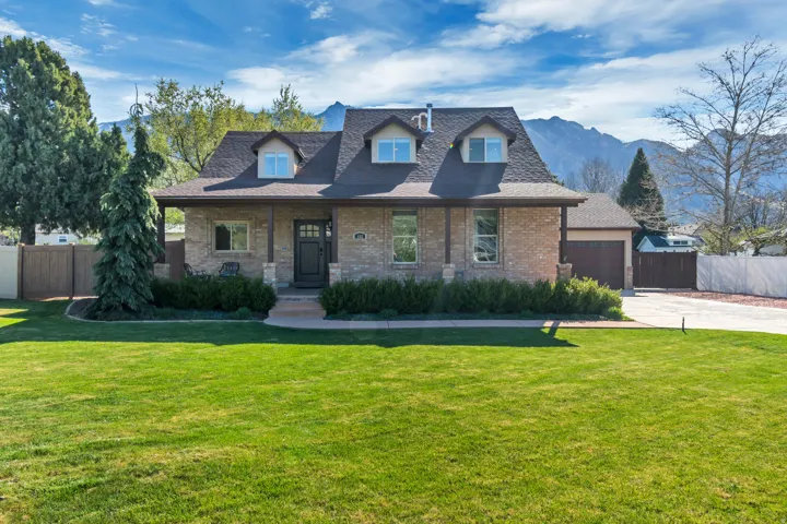 View of front of home with covered porch, brick siding, roof with shingles, and a garage