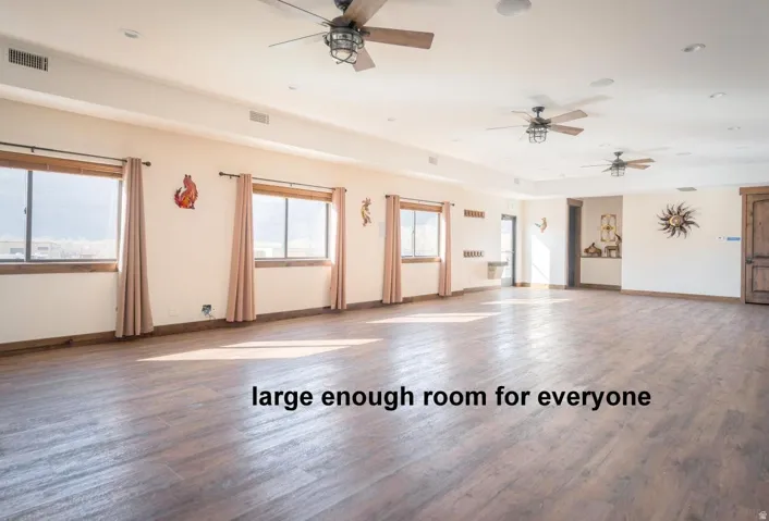 For large groups of friends. Unfurnished room featuring dark wood finished floors, healthy amount of natural light, a ceiling fan, and recessed lighting