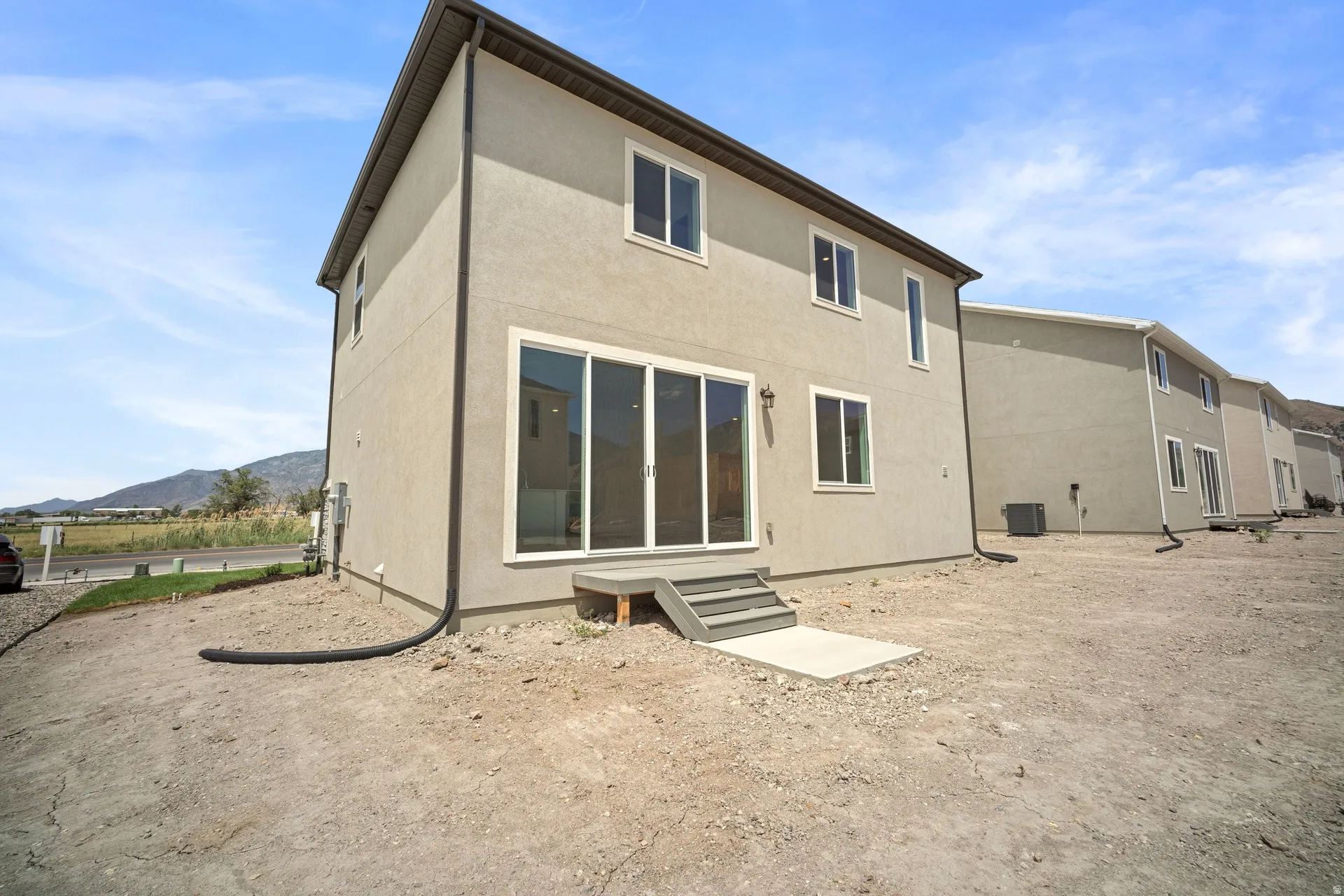Rear exterior featuring neutral stucco siding, a multi-pane sliding glass door, and white frame windows