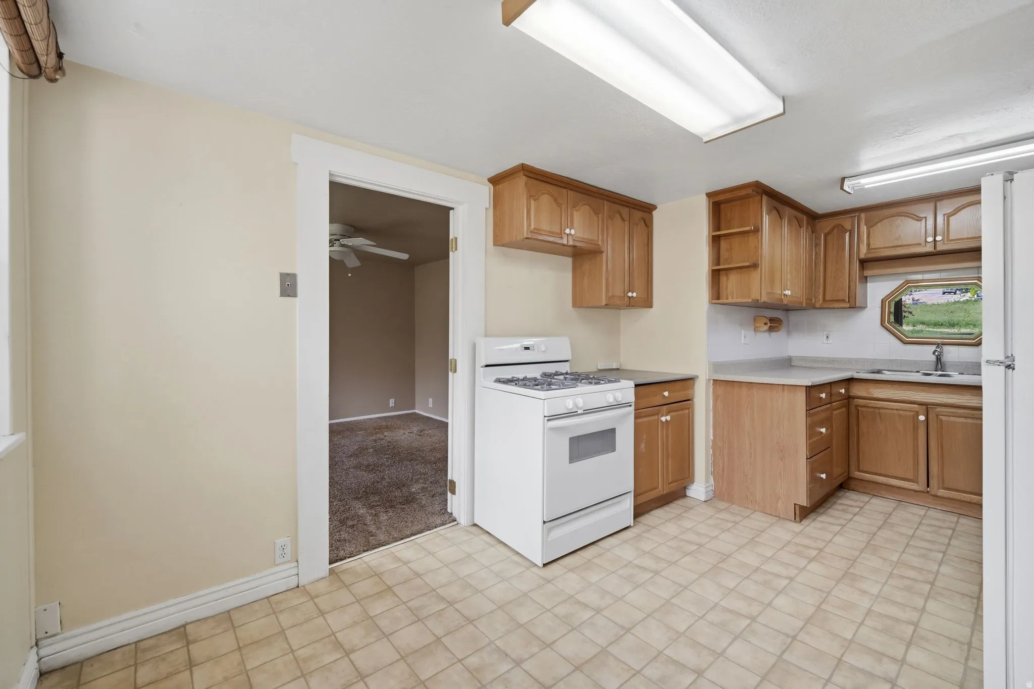 Kitchen featuring white appliances, light countertops, wood finish cabinetry, and light carpet