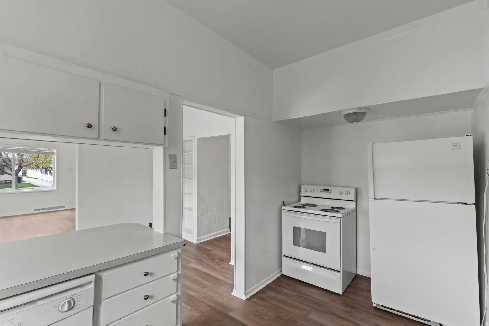 Kitchen featuring white appliances, white cabinetry, vinyl floors, light countertops, and crown molding