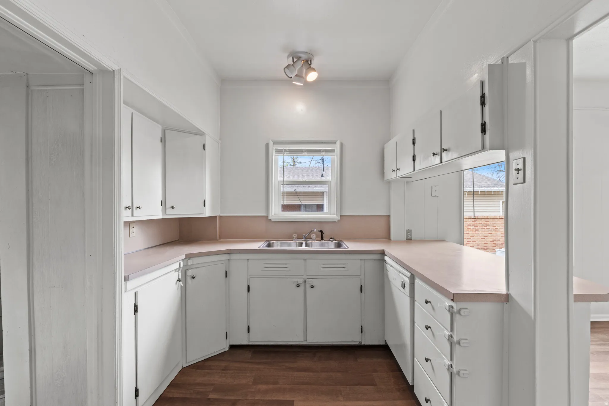 Kitchen with light countertops, vinyl flooring, white cabinets, and dishwasher