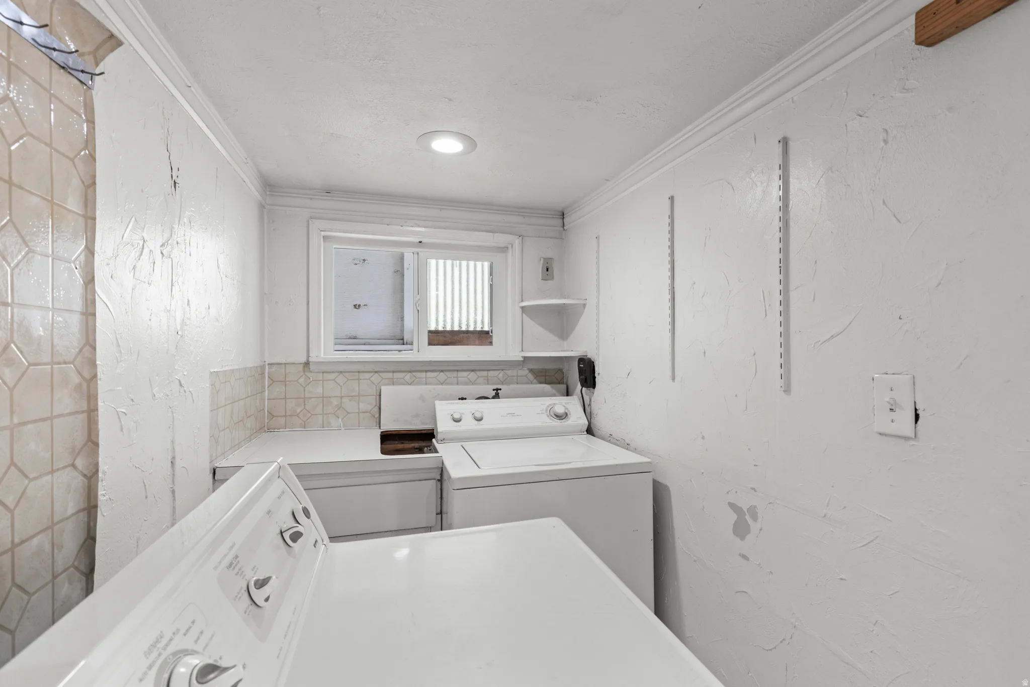 Laundry area with ornamental molding, a textured wall, and washing machine and clothes dryer