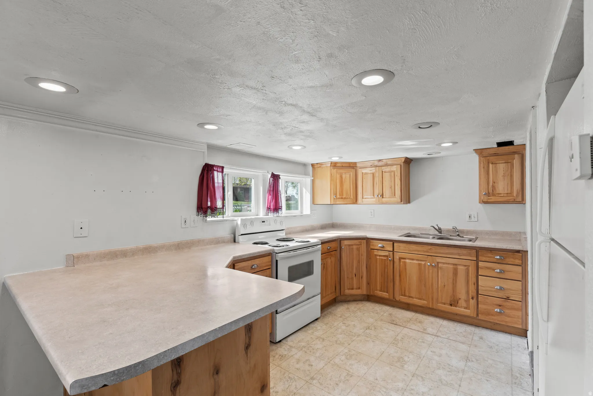 Kitchen with a peninsula, white appliances, light countertops, light floors, and a textured ceiling