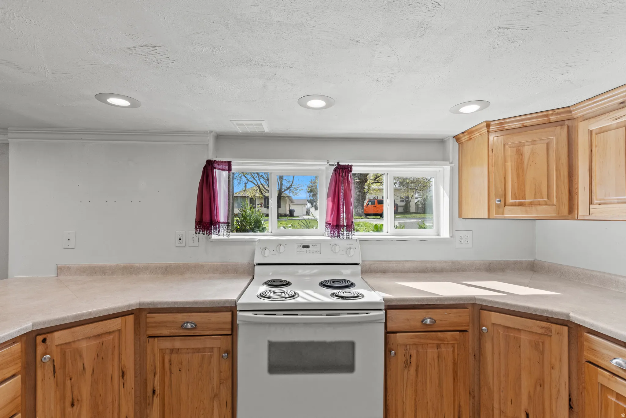 Kitchen with electric stove, light countertops, recessed lighting, and a textured ceiling
