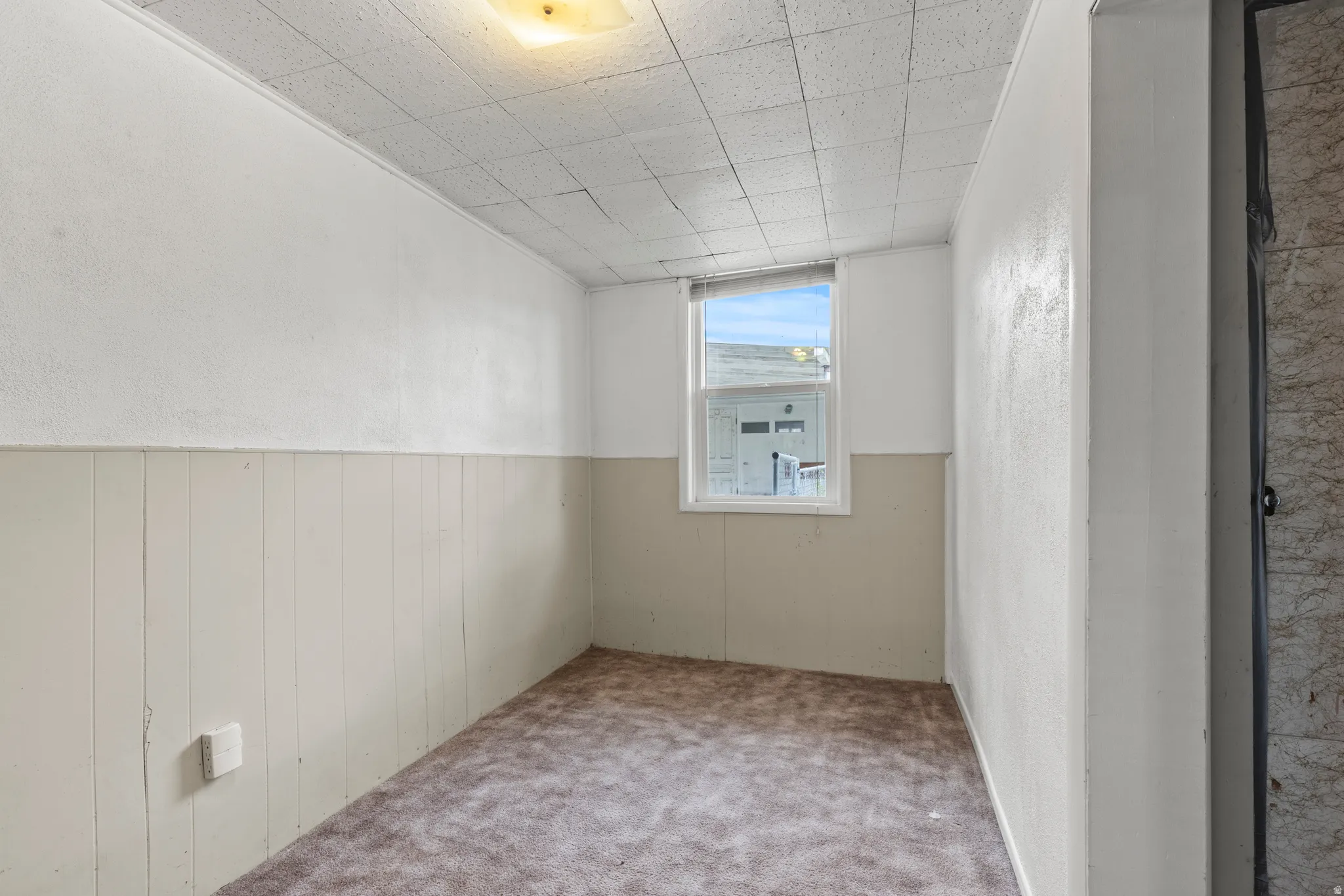 Empty room with carpet floors, a textured wall, wainscoting, and wood walls