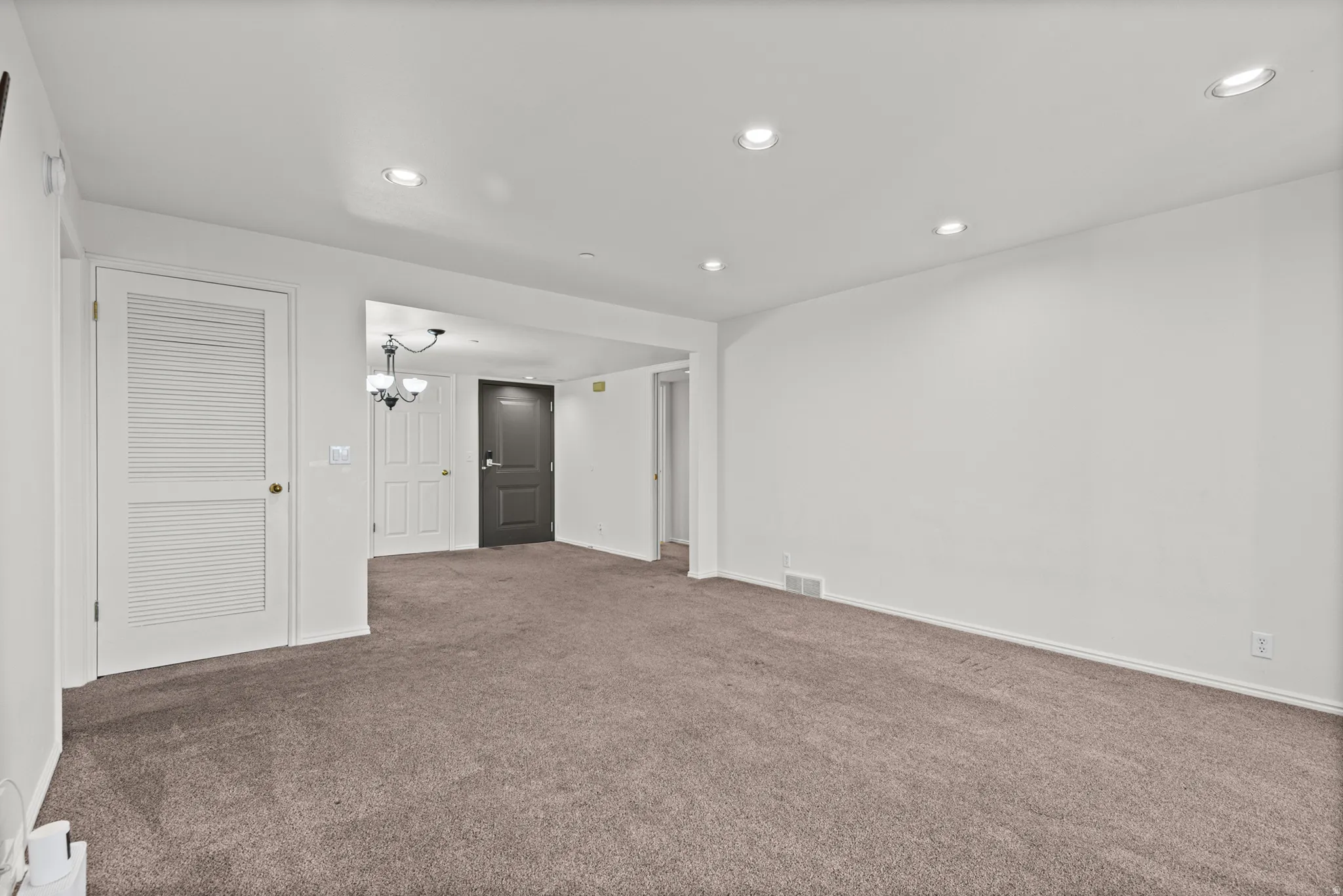 Spacious carpeted recreation room featuring recessed ceiling lighting, white louvered closet doors, and neutral wall finishes