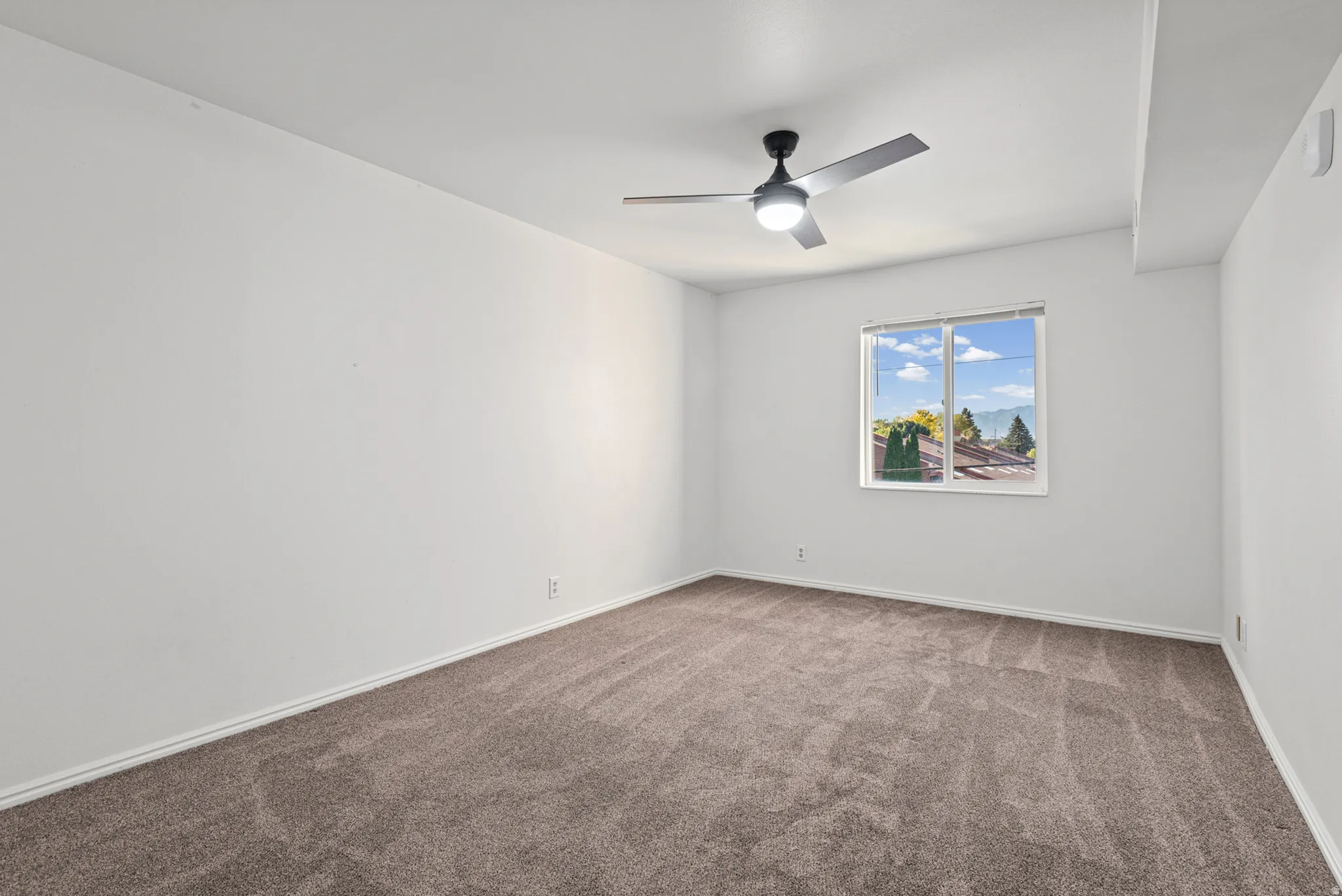 Bright bedroom with carpet flooring, ceiling fan with integrated lighting, and large window framing natural daylight and outdoor scenery