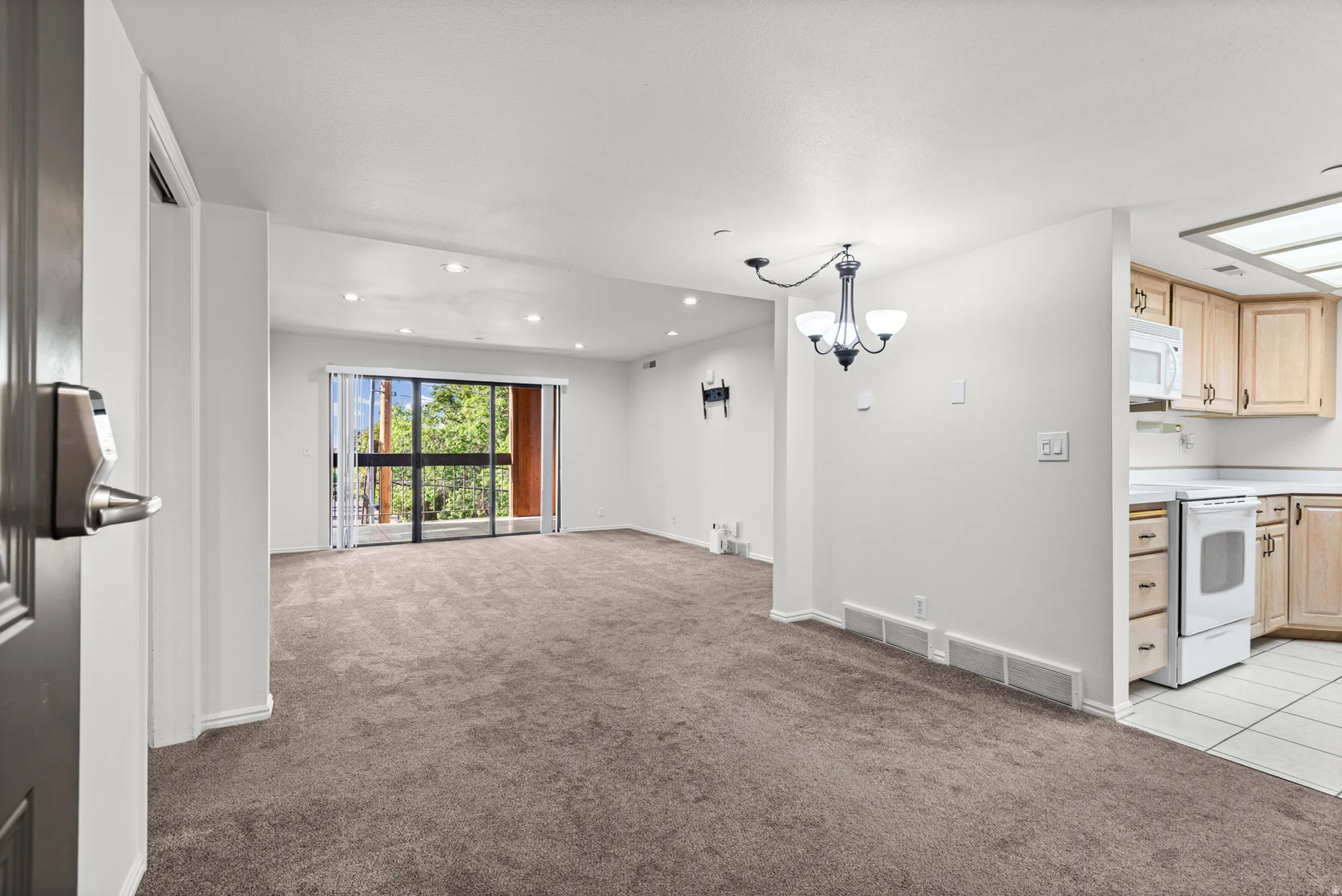 Spacious living area with sliding glass doors, recessed lighting, and carpet flooring