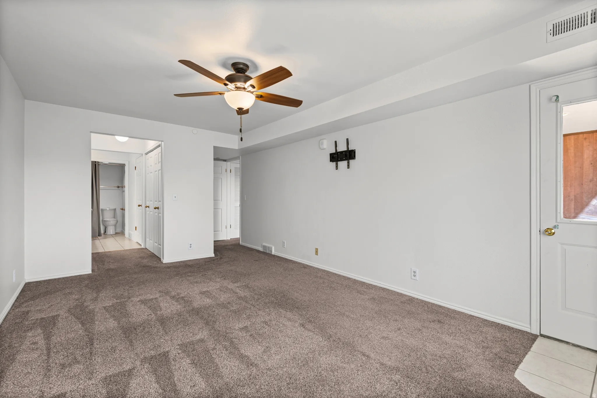 Carpeted flooring, ceiling fan with integrated lighting, wall-mounted fixture, and white interior doors