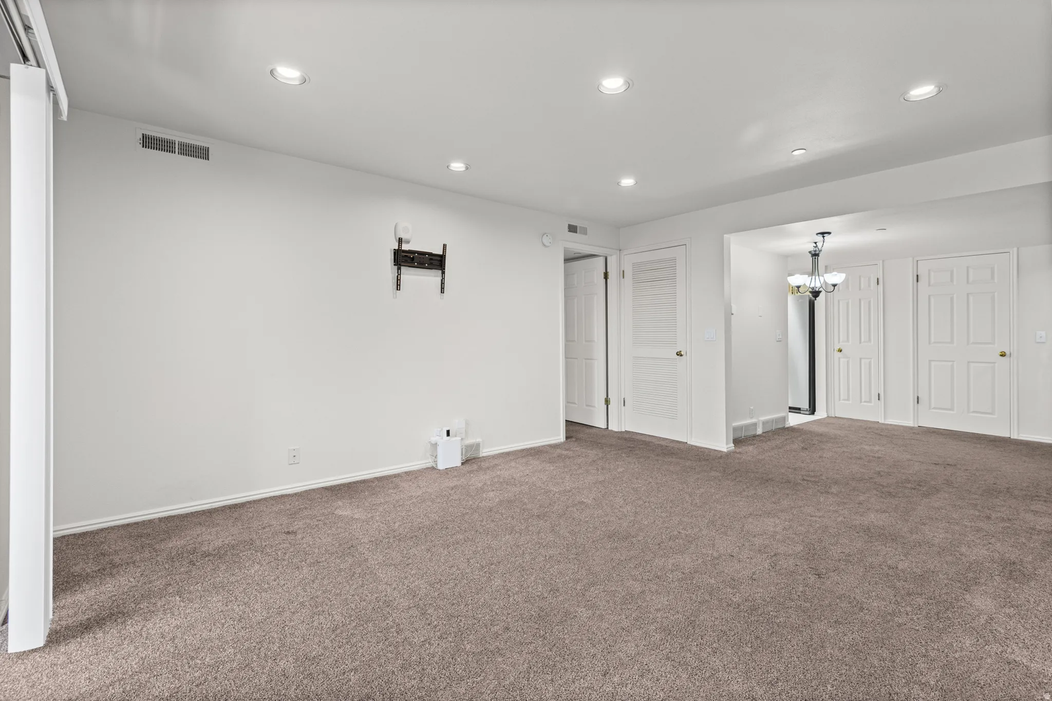 Recessed lighting, neutral-toned carpeting, white interior doors, and a chandelier with glass shades