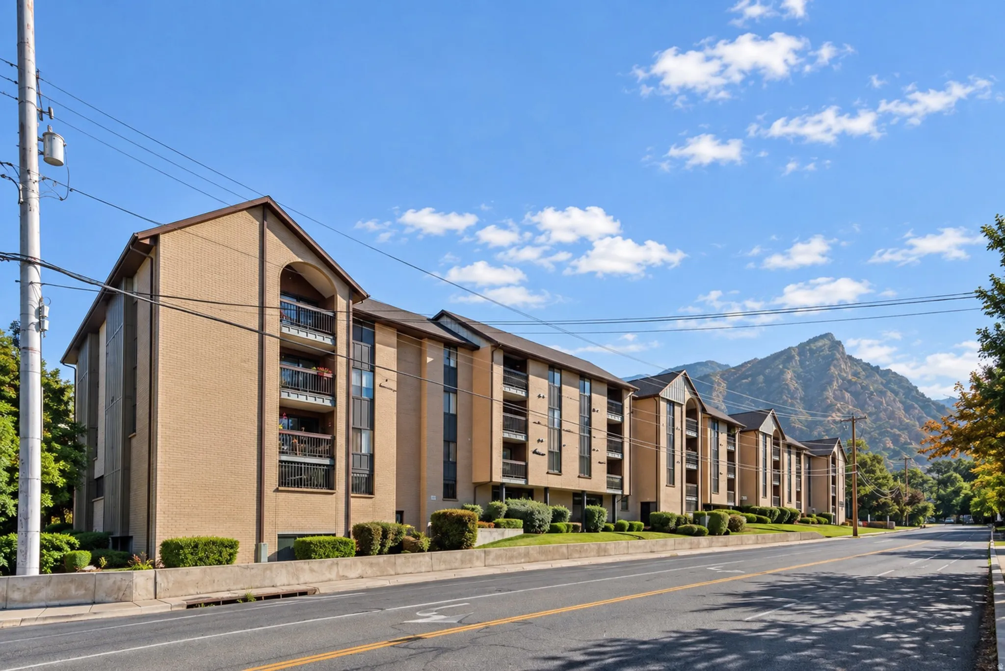 Brick exterior building with multiple balconies, established landscaping, and a mountainous backdrop