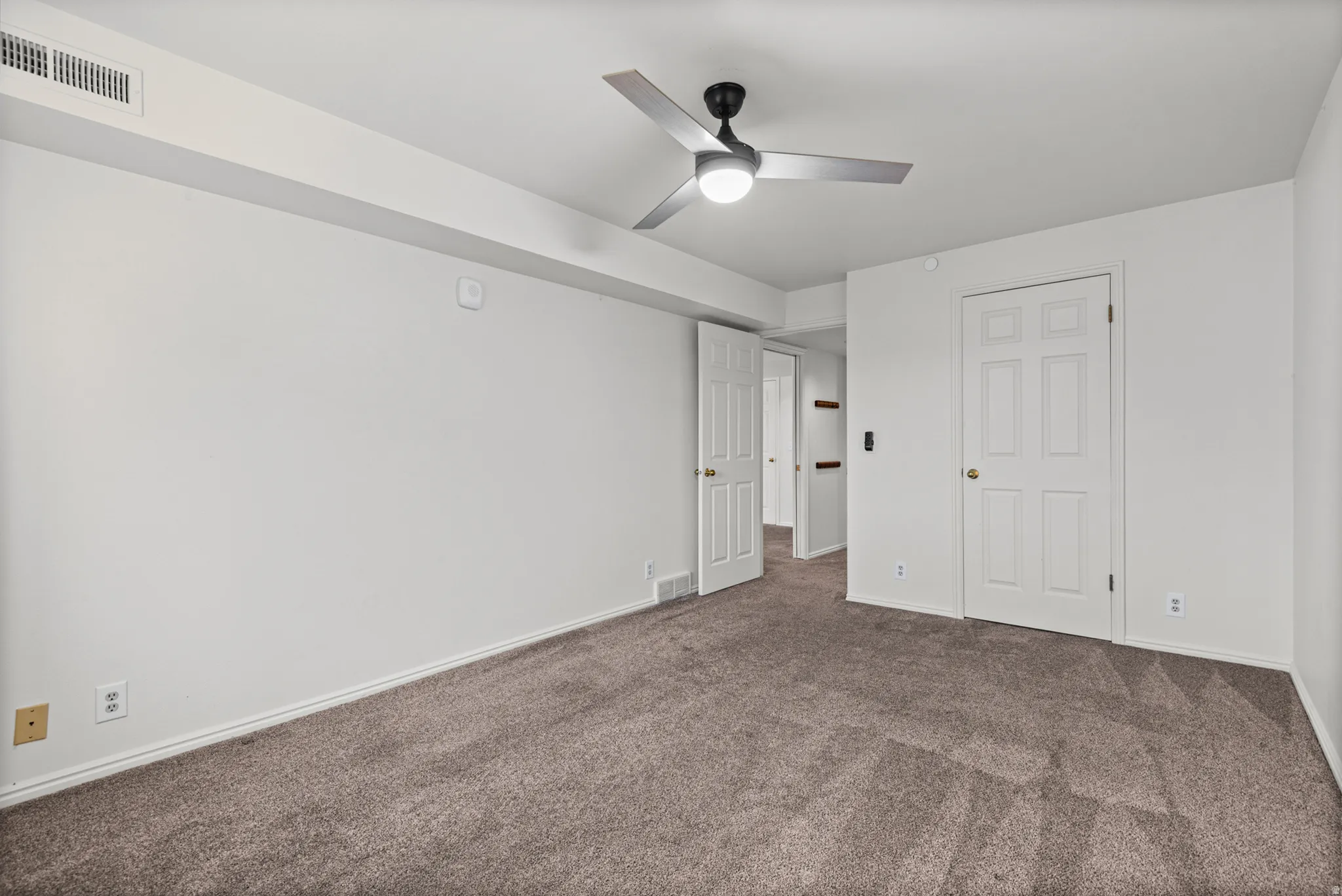 Spacious bedroom featuring neutral wall finishes, carpeted flooring, a ceiling fan with integrated lighting, and multiple closet spaces with six-panel doors