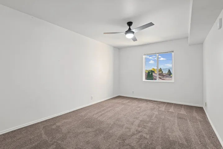 Bright bedroom with carpet flooring, ceiling fan with integrated lighting, and large window framing natural daylight and outdoor scenery