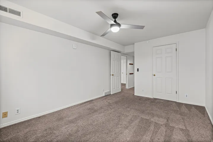 Spacious bedroom featuring neutral wall finishes, carpeted flooring, a ceiling fan with integrated lighting, and multiple closet spaces with six-panel doors