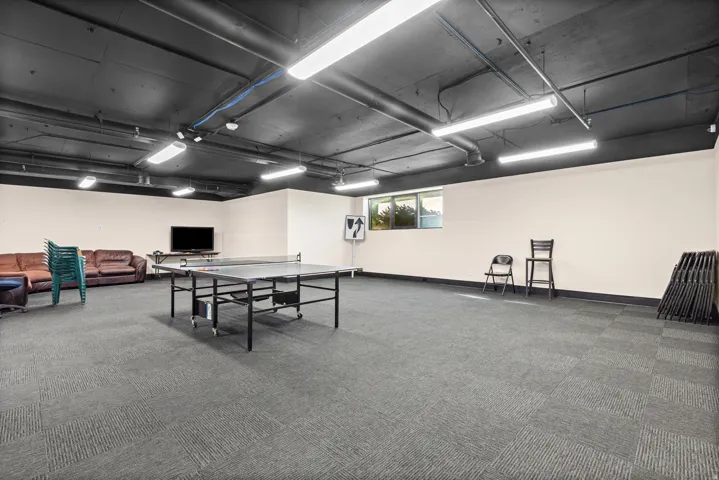 Expansive recreational space featuring carpet tile flooring, exposed ductwork, and fluorescent lighting