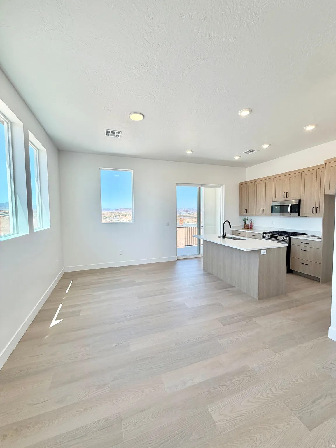 Open-concept living space featuring wood-finish flooring, recessed lighting, and ample natural light from multiple windows and a sliding glass door