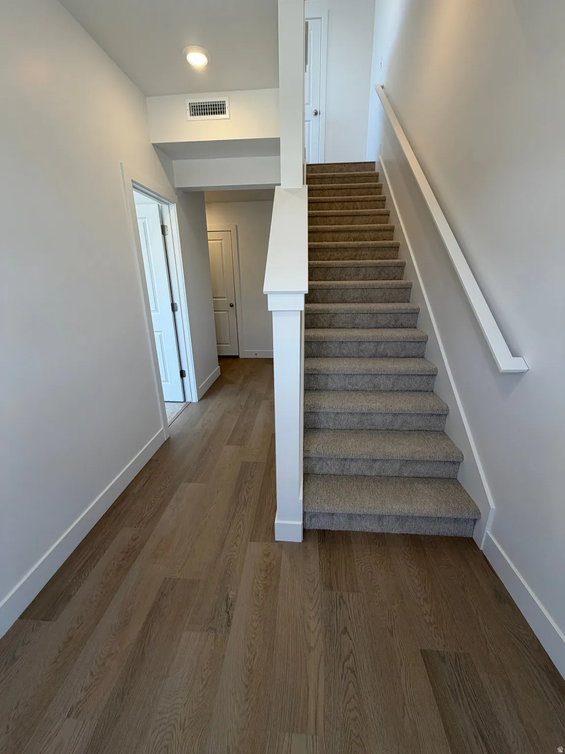 Entryway featuring wood-finish flooring, a carpeted staircase with white risers, and contemporary white walls