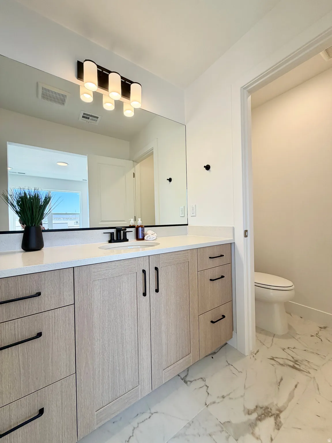 Spacious vanity featuring light wood-finish cabinetry with matte black hardware, a pristine white countertop, and an integrated rectangular sink