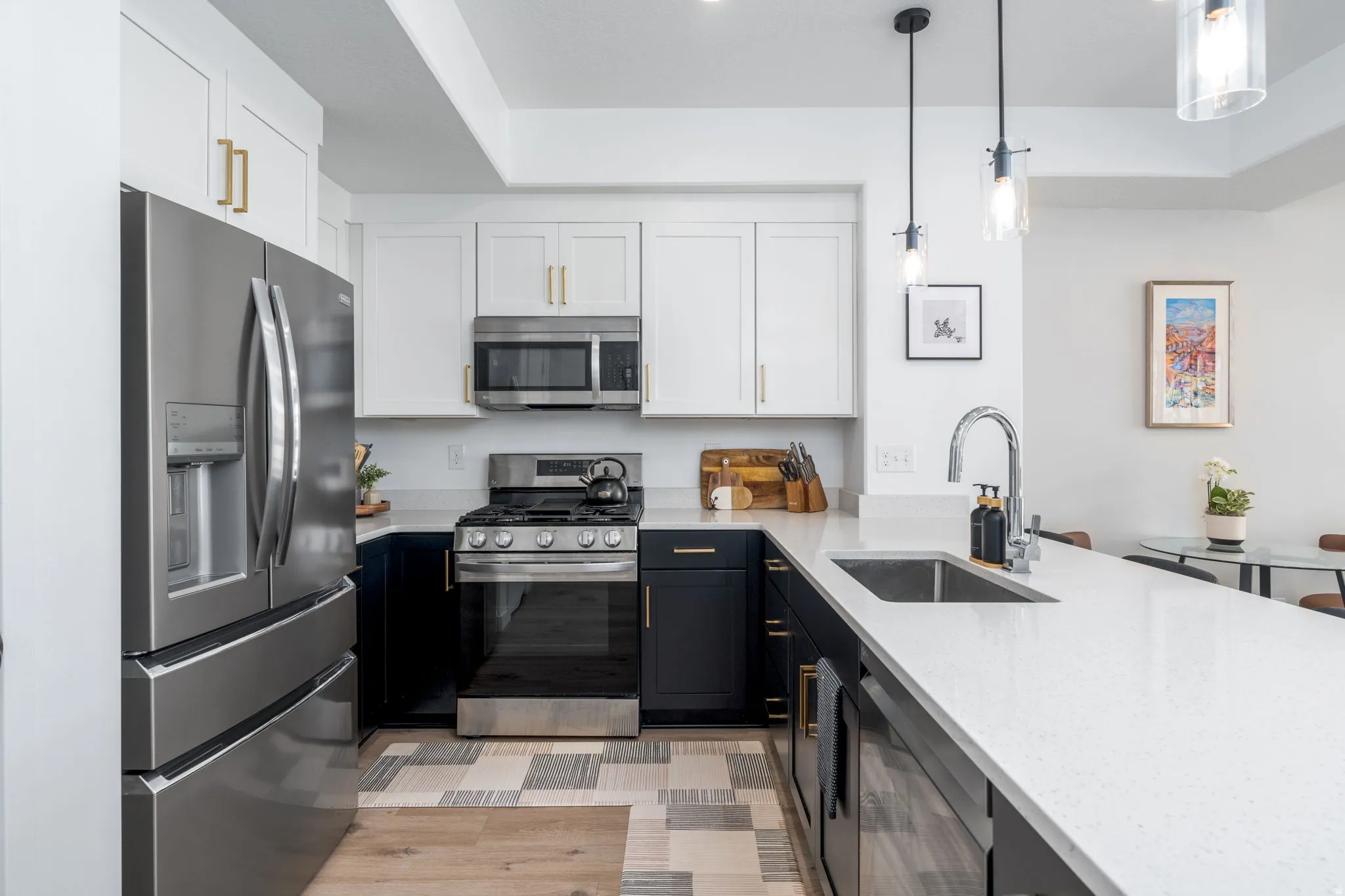 Dual tone kitchen with two tone cabinets, stainless steel appliances, light stone countertops, a peninsula, and pendant lighting