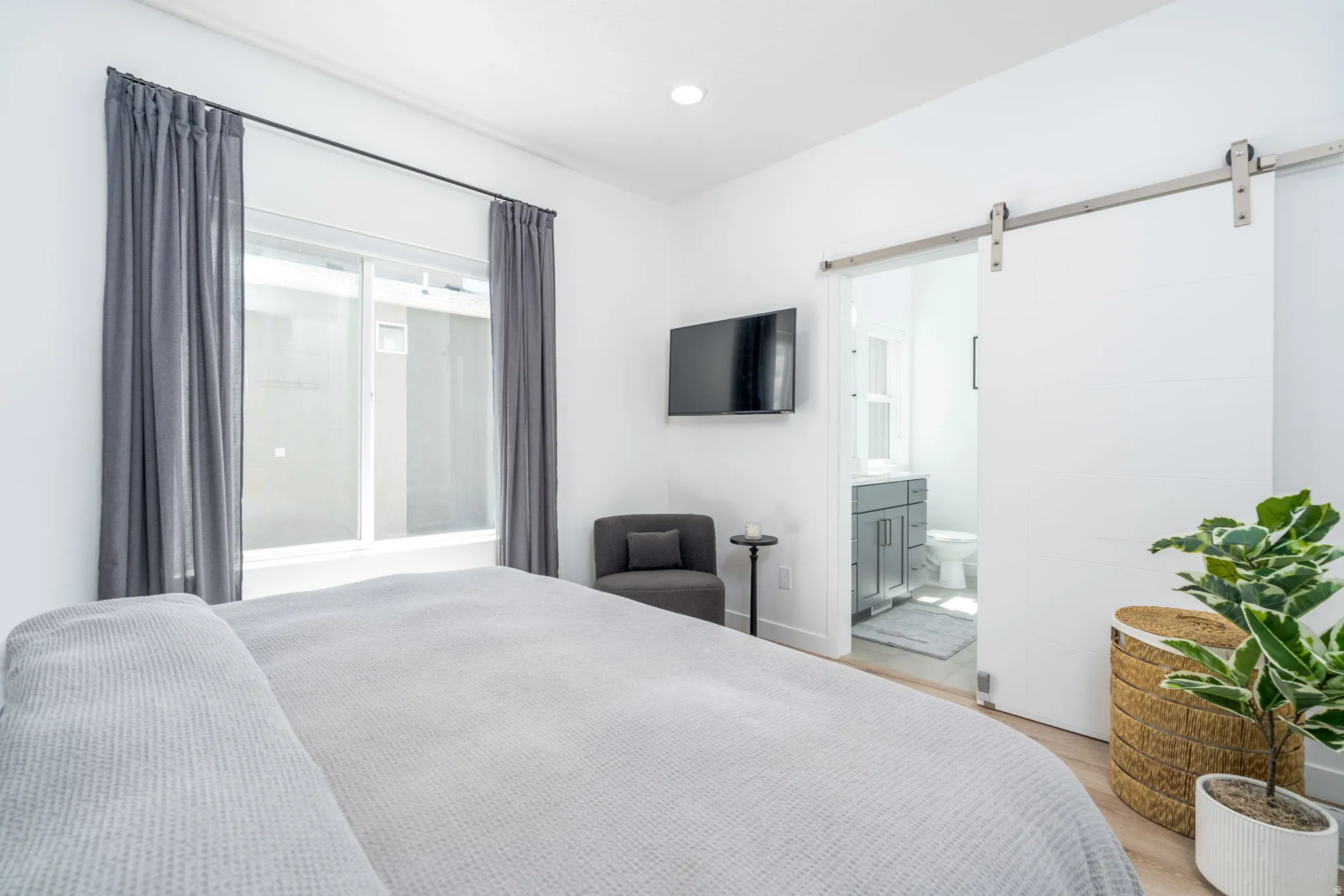 Bedroom featuring a barn door, light wood-style flooring, connected bathroom, and recessed lighting